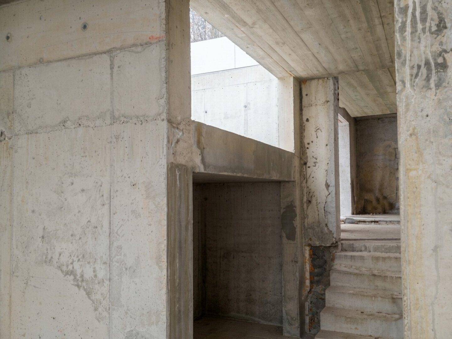 Rohbau-Innenbereich mit Sichtbetonwänden und -decken sowie einer unfertigen Treppe.