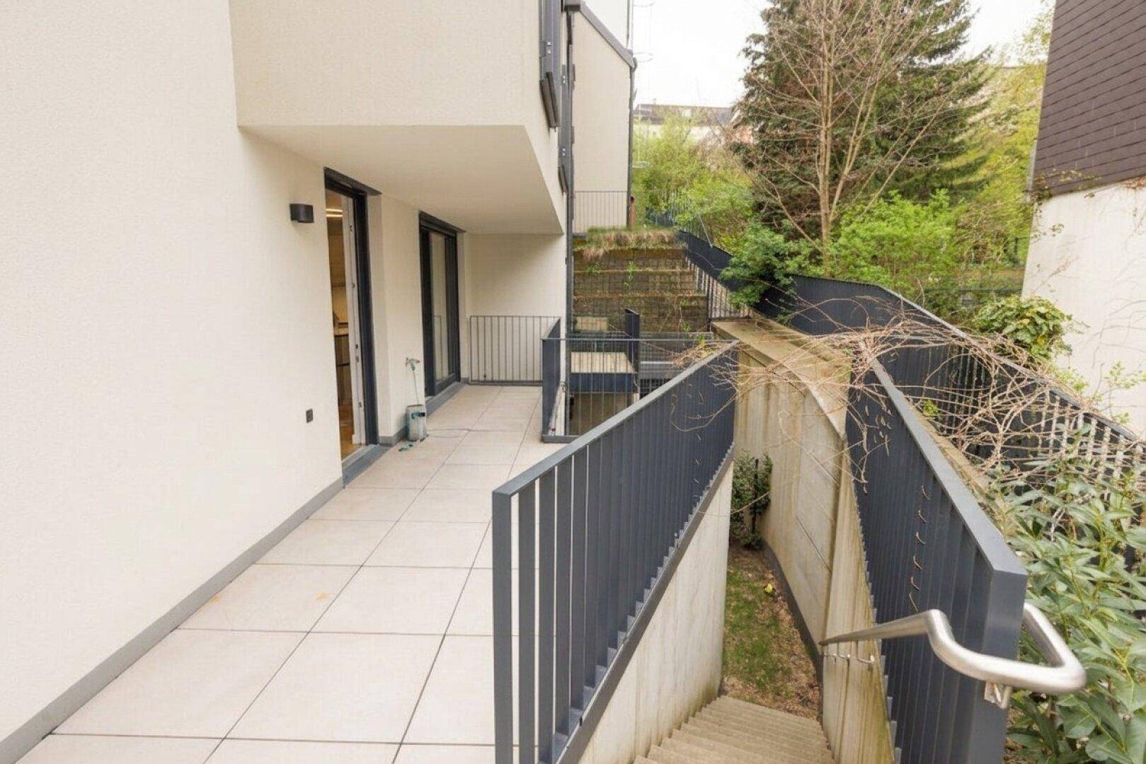 Lange, geflieste Terrasse mit modernem Geländer und Zugang zu einer Außentreppe.