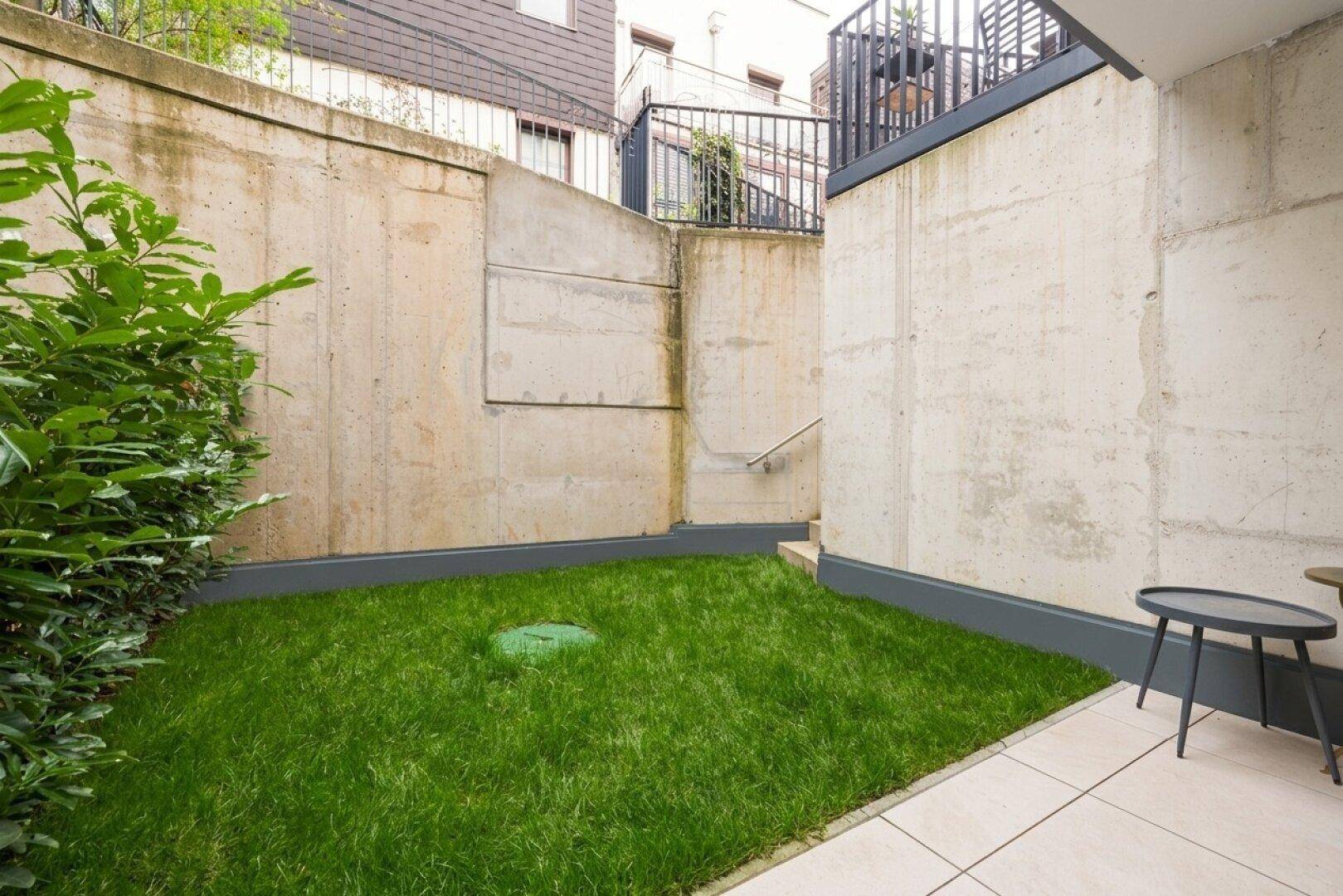 Kleiner, gepflegter Rasenbereich im Garten, umgeben von Betonwänden und Sträuchern.