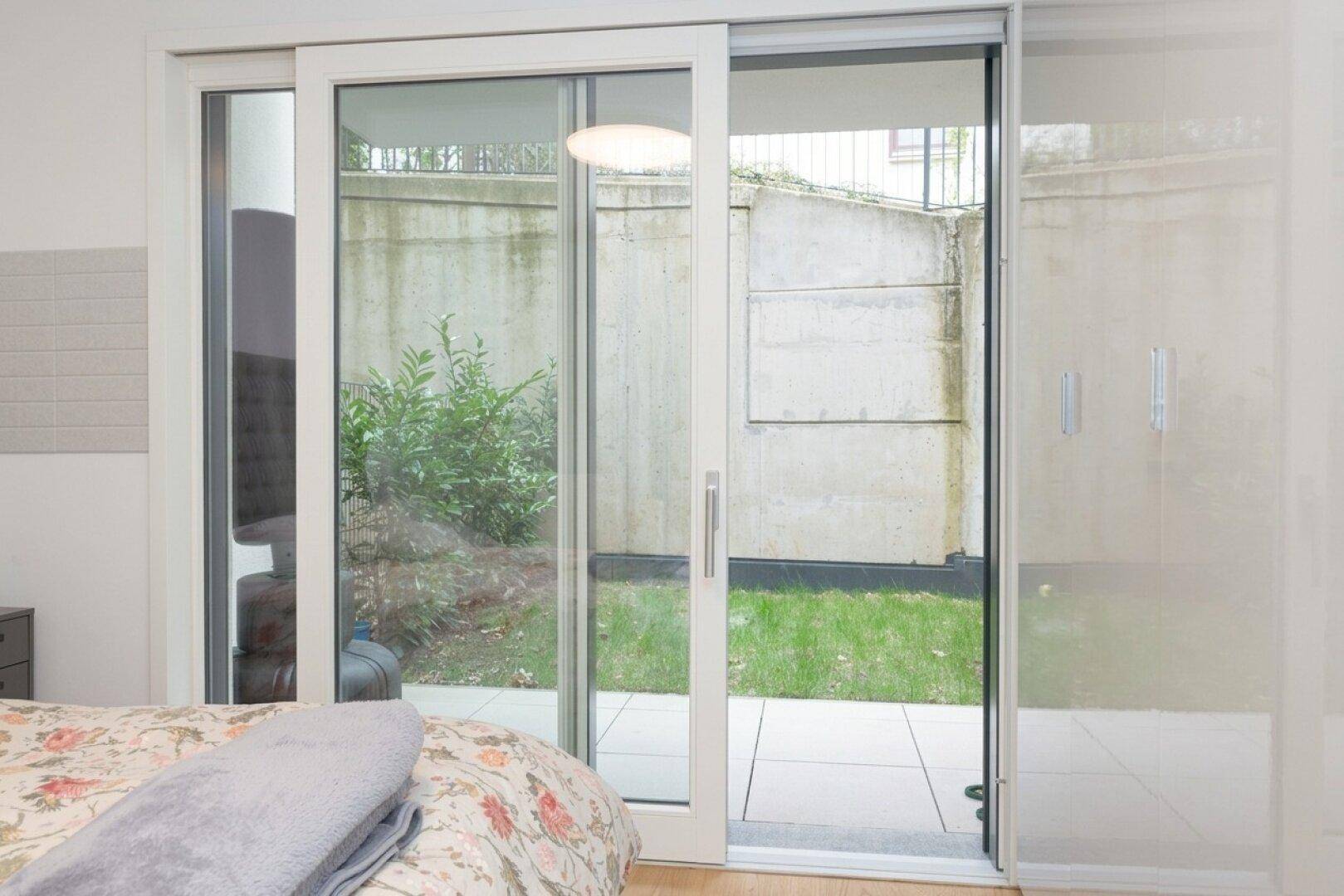 Schlafzimmer mit großen Schiebetüren, die Zugang zu einem kleinen Gartenbereich bieten.