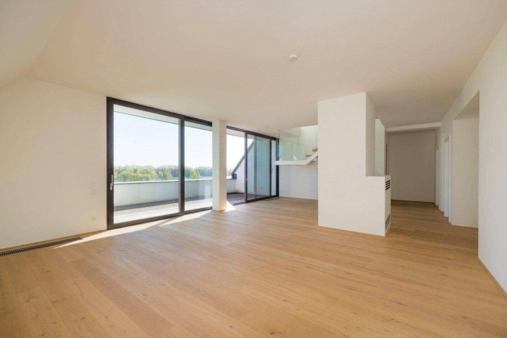 Geräumiger, heller Wohnbereich mit Holzboden und Zugang zu mehreren Balkonen mit Seeblick.