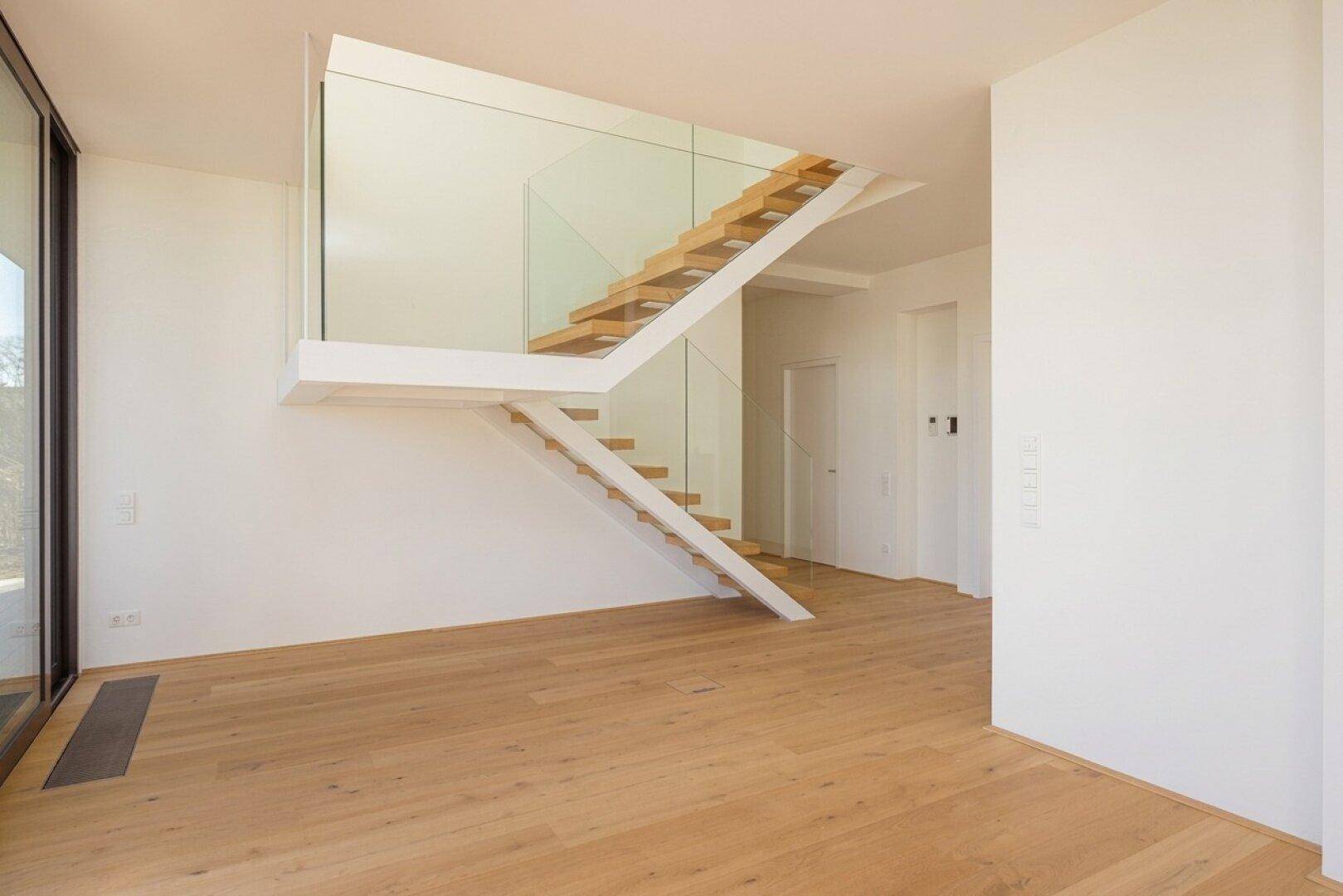 Moderner Treppenaufgang mit schwebenden Holzstufen und elegantem Glasgeländer in einem hellen Raum.