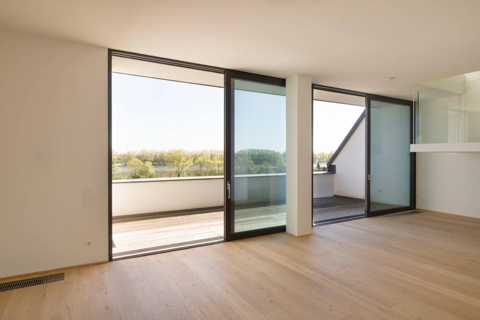 Heller Wohnraum mit großen Schiebetüren, die auf eine Terrasse mit weitem Blick auf den See führen.