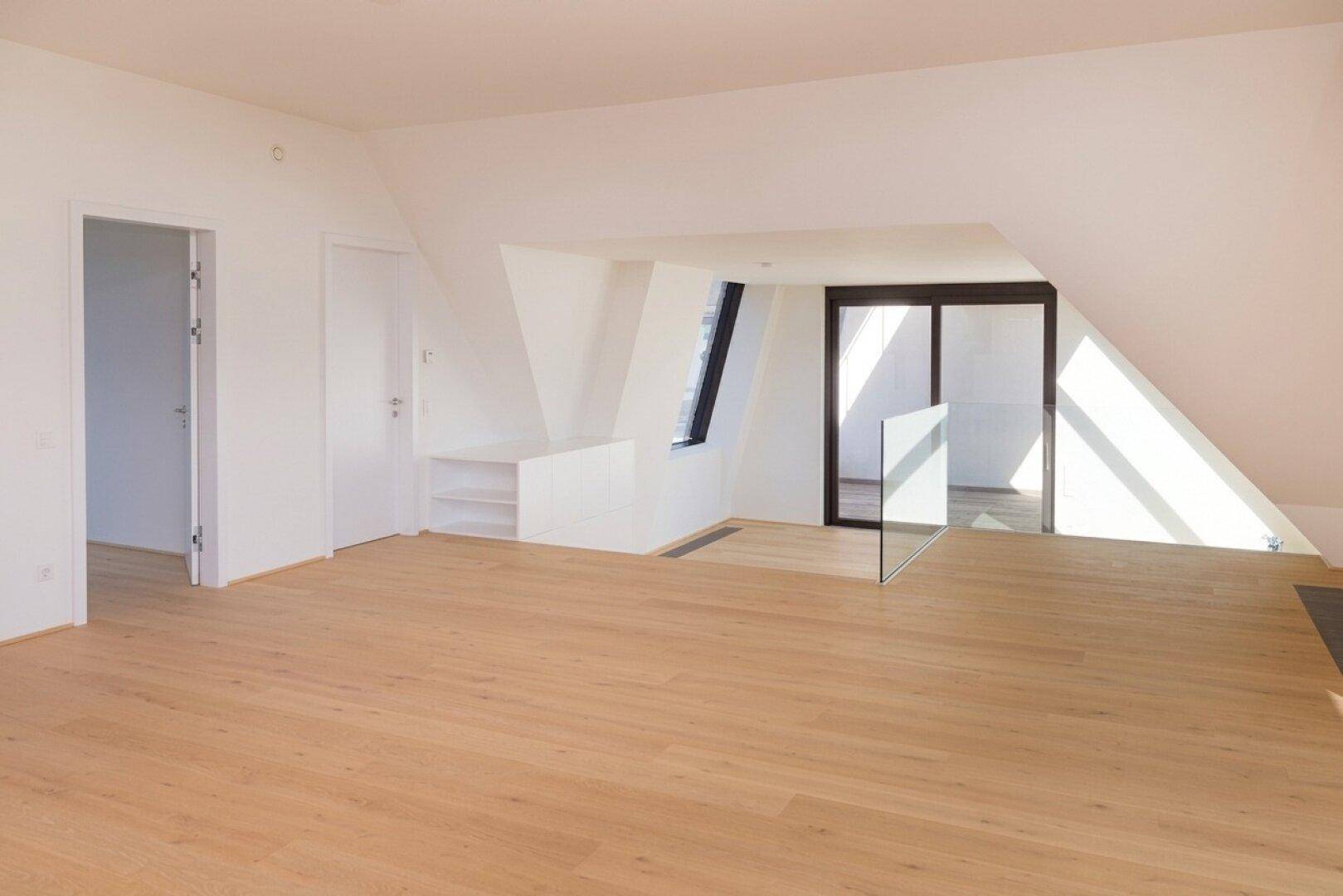 Heller Dachgeschossraum mit schrägen Wänden, Holzboden und großen Dachfenstern, die viel Licht hereinlassen.