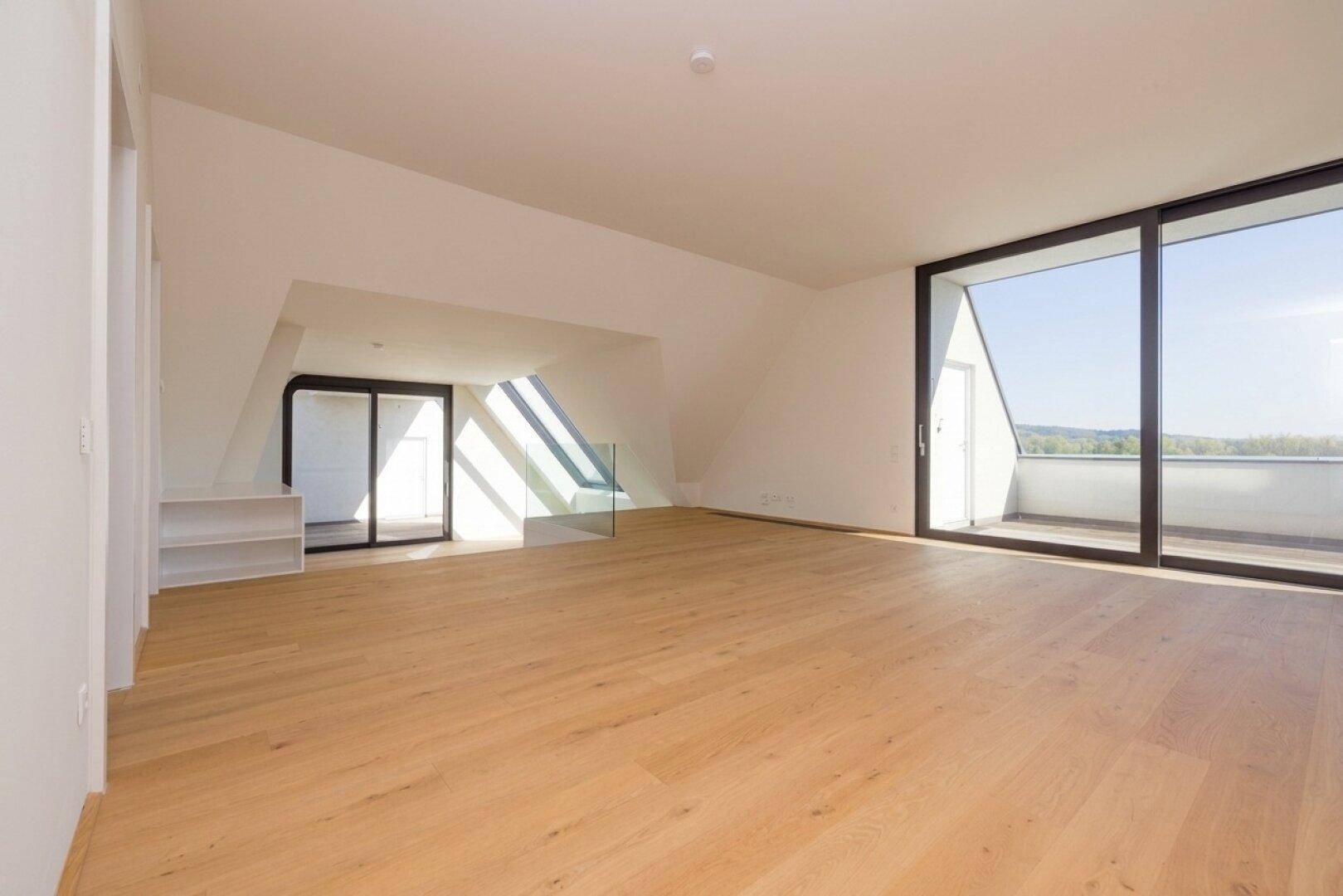 Geräumiger Dachgeschossraum mit schrägen Decken, Holzboden und Zugang zu einem Balkon mit schöner Aussicht.