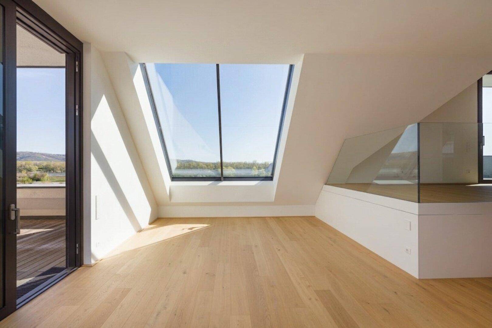 Heller Dachgeschossraum mit beeindruckendem, großem Schrägfenster und Holzboden, das viel Tageslicht bietet.