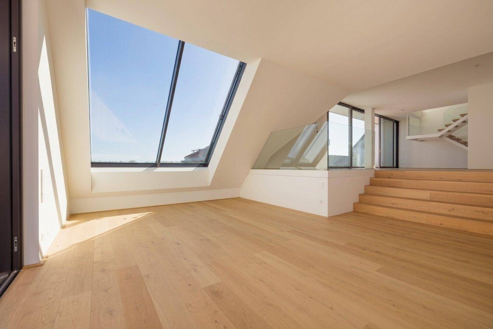 Offener Dachgeschossbereich mit Holzboden, Stufen zu einer unteren Ebene und einem großen Schrägfenster.