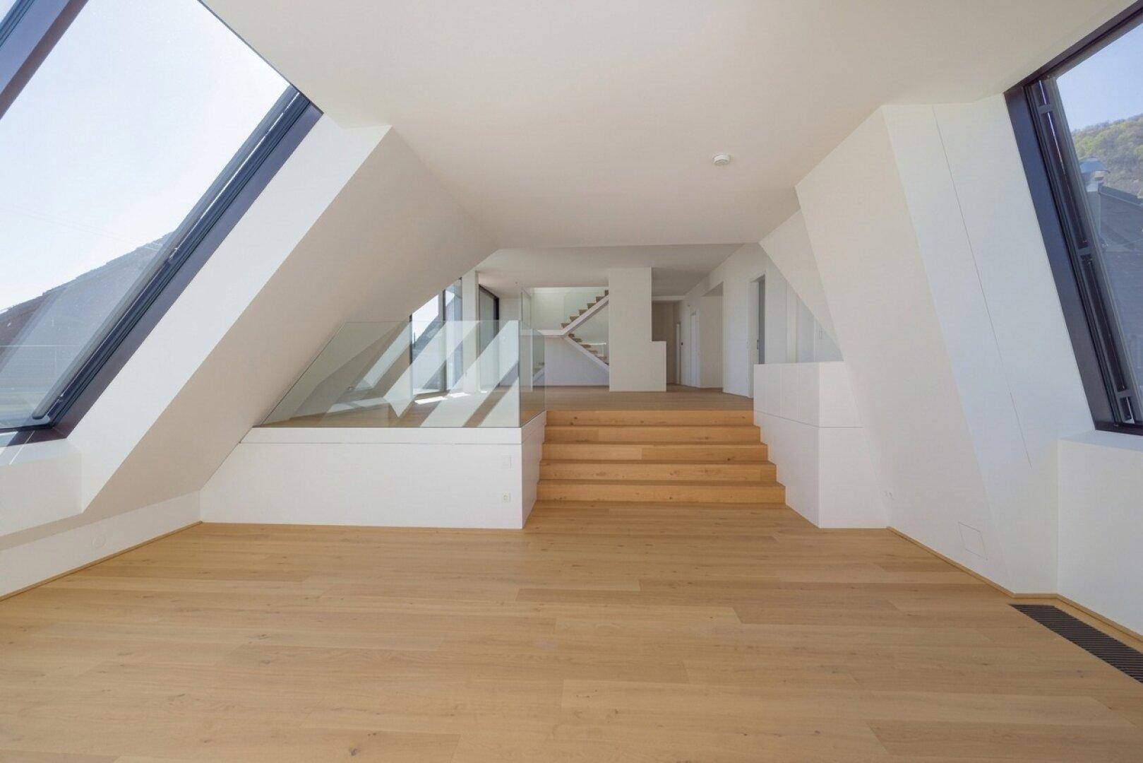 Geräumiger Dachgeschossbereich mit Holzboden, Stufen und mehreren großen Schrägfenstern für viel Licht.