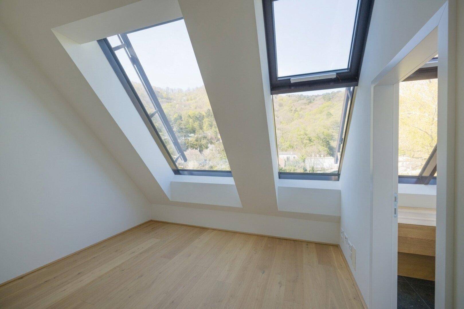 Dachgeschosszimmer mit Holzboden, schrägen Wänden und zwei großen Schrägfenstern, die viel Licht spenden.