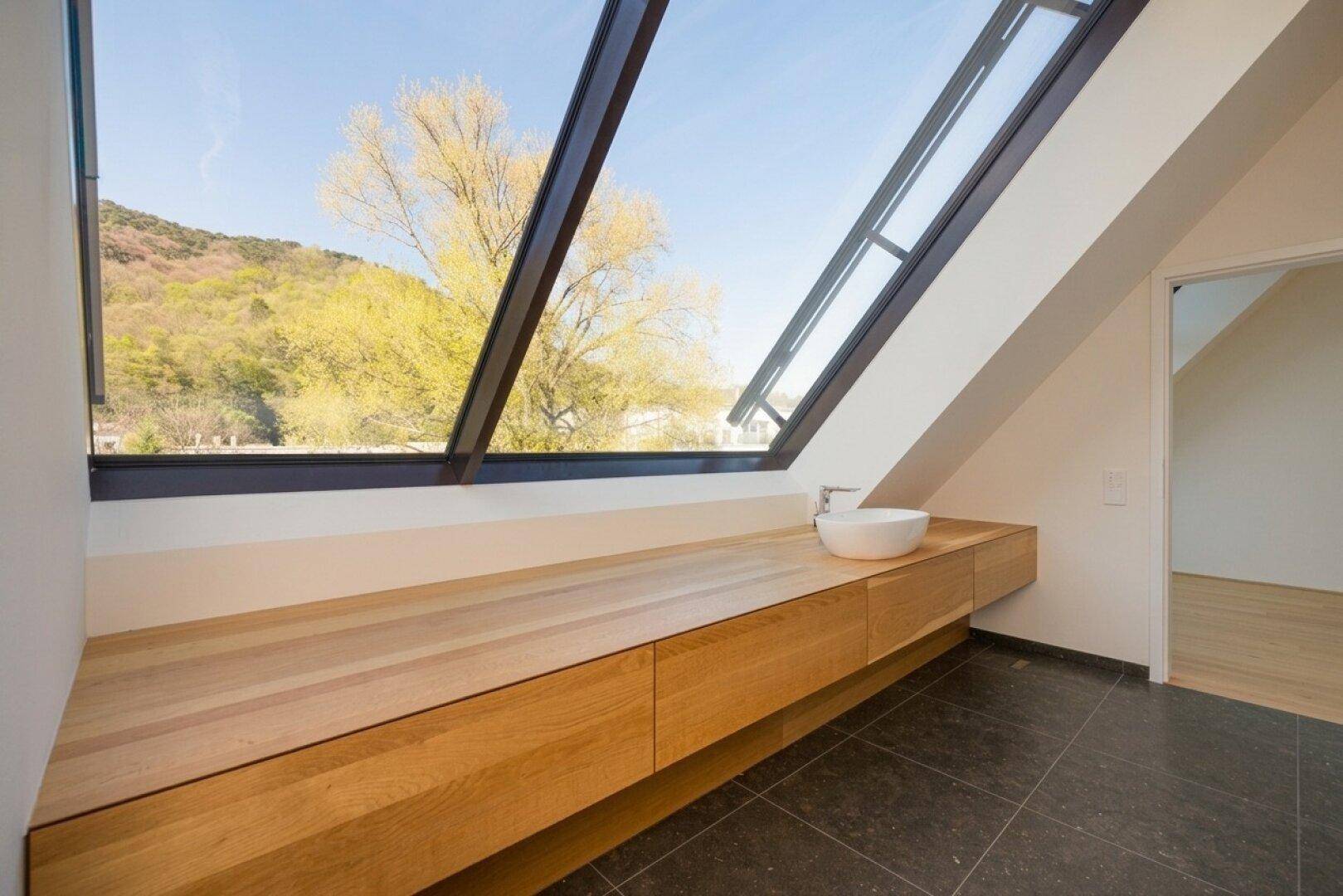 Modernes Badezimmer mit Holzwaschtisch, Aufsatzwaschbecken und großem Schrägfenster mit Blick ins Grüne.