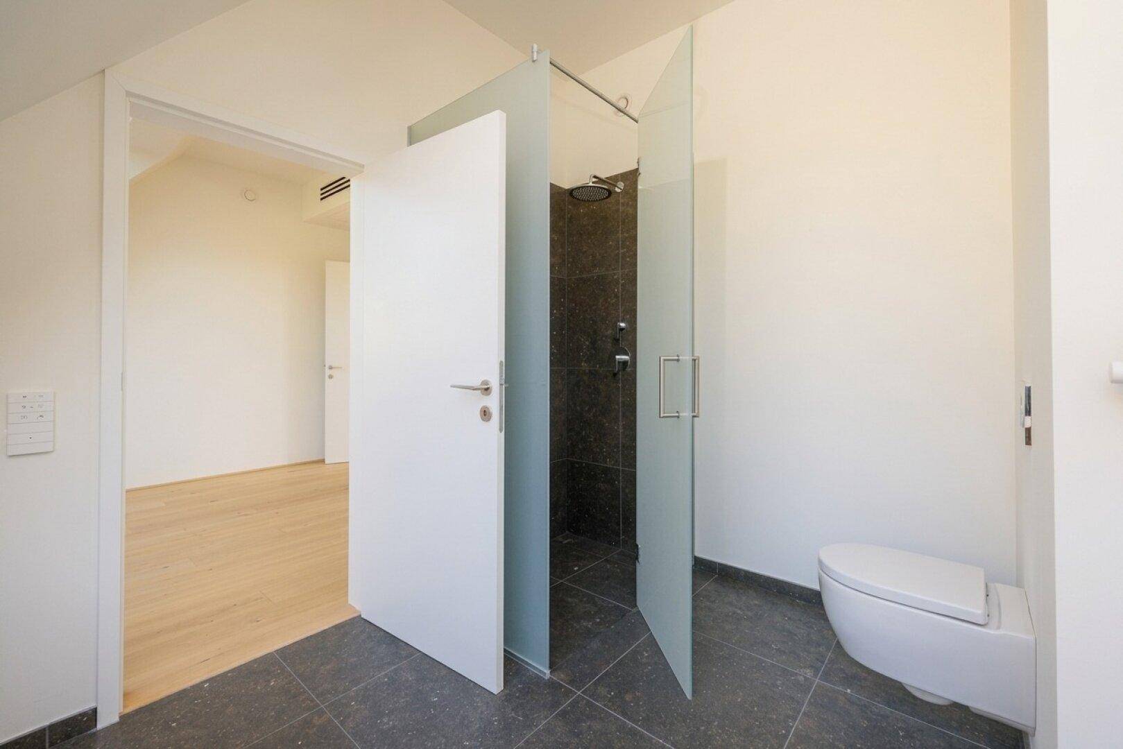 Modernes Badezimmer mit wandhängendem WC und einer begehbaren Dusche mit eleganten Glastüren.