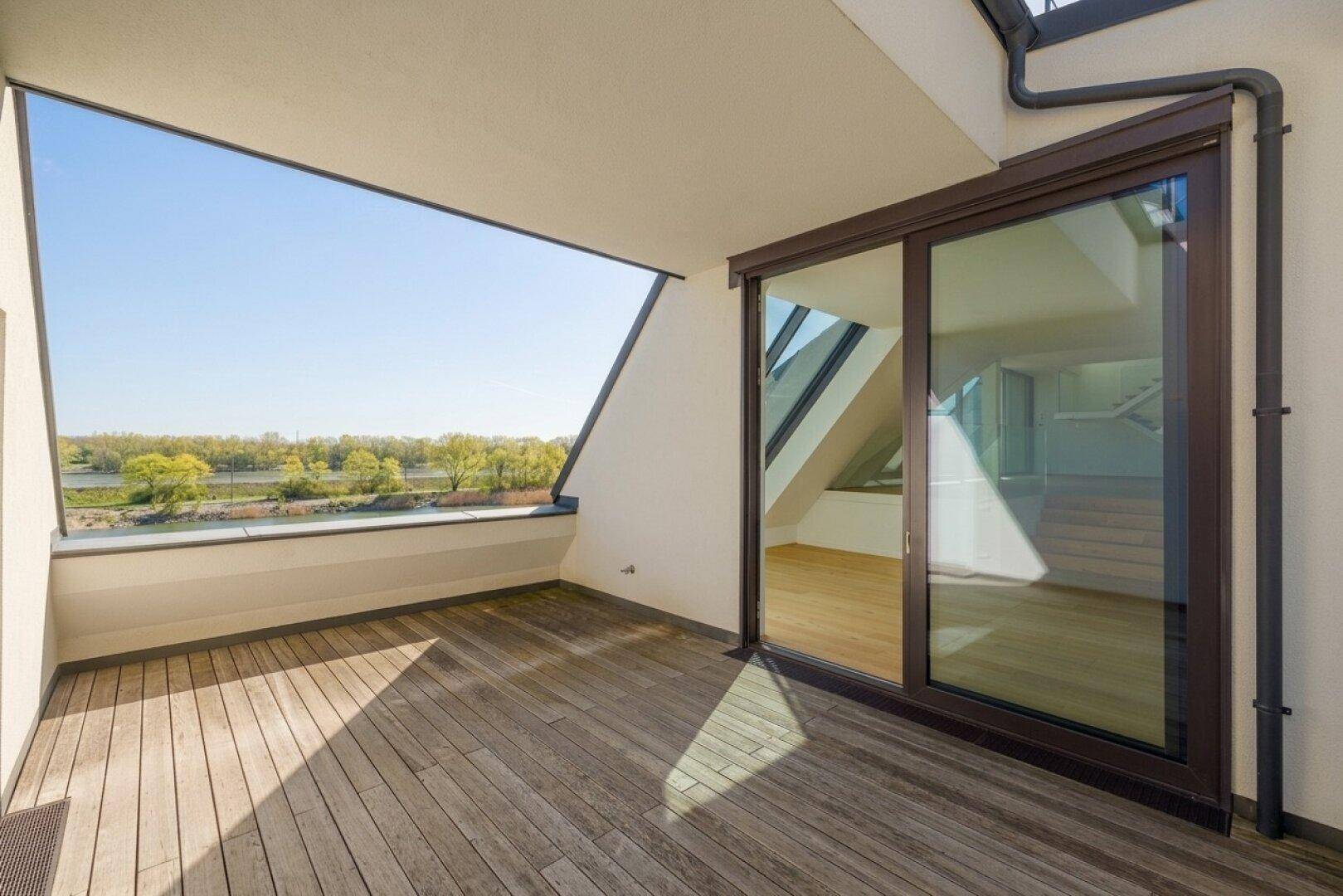 Großer Balkon mit Holzdeck und Schiebetüren zum Innenbereich, bietet einen schönen Blick auf den See.