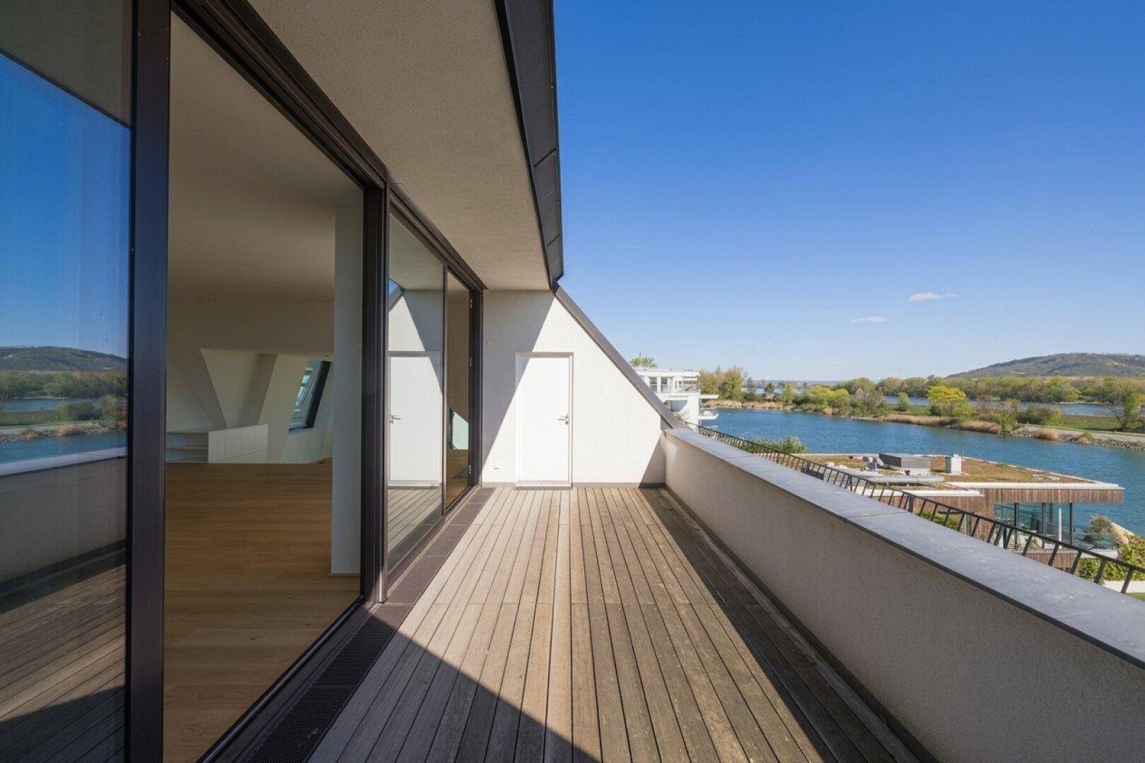 Langer Balkon mit Holzdeck und Panoramablick auf den See und die umliegenden Hügel.