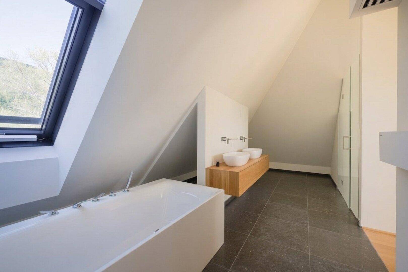 Luxuriöses Badezimmer mit freistehender Badewanne, Doppelwaschbecken und großem Schrägfenster mit Aussicht.