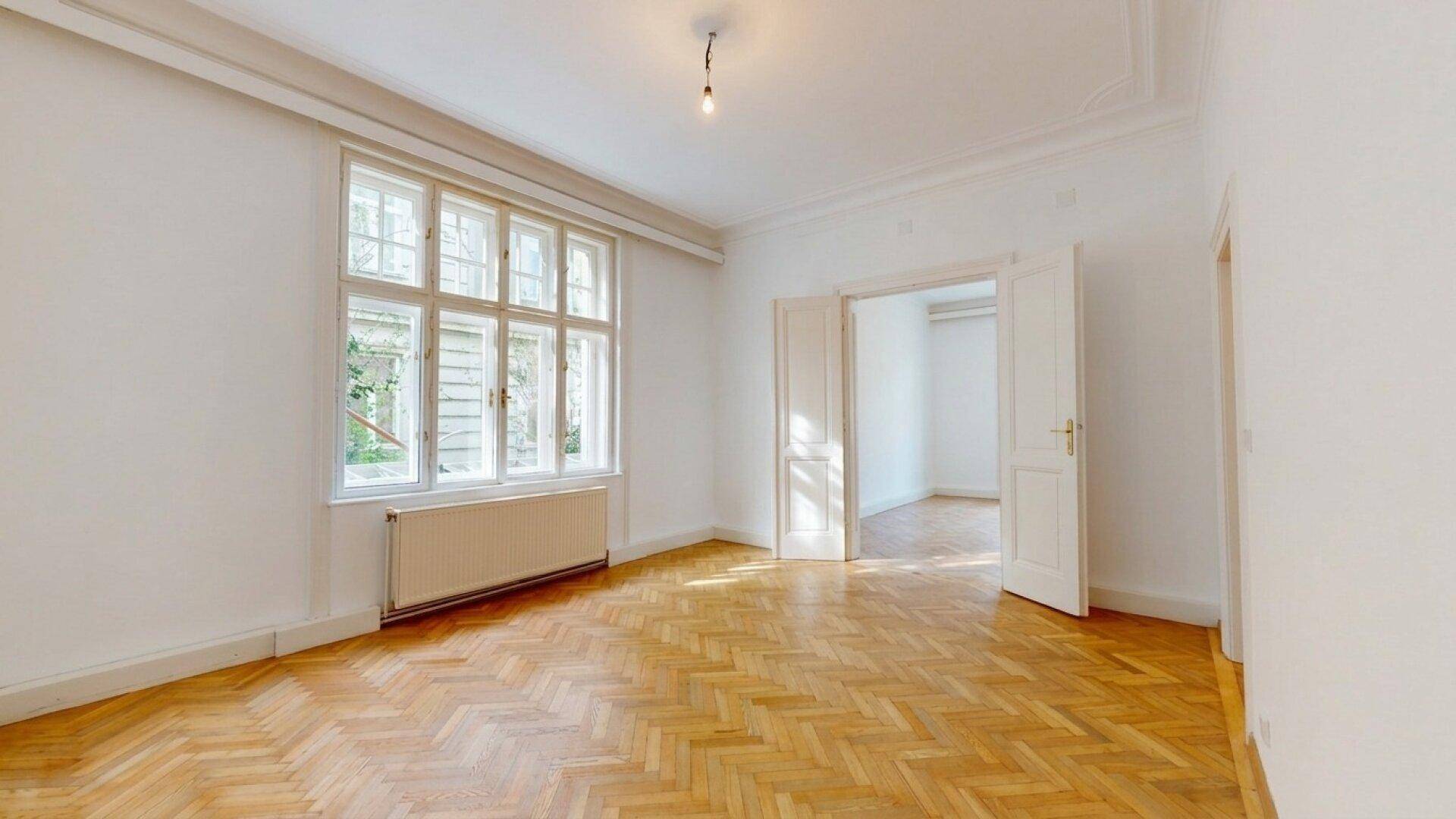 Geräumiges, leeres Zimmer mit Fischgrätparkett und hohen Decken, ideal für individuelle Gestaltung.