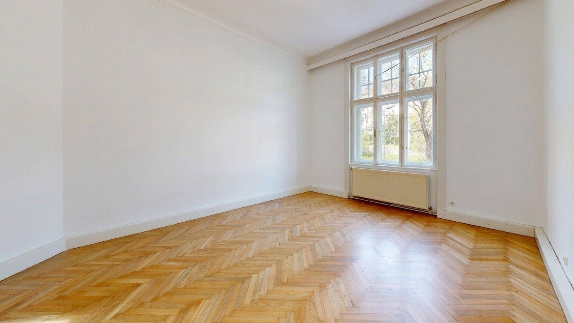 Geräumiges Zimmer mit Fischgrätparkett und einem großen Fenster, das eine angenehme Atmosphäre schafft.