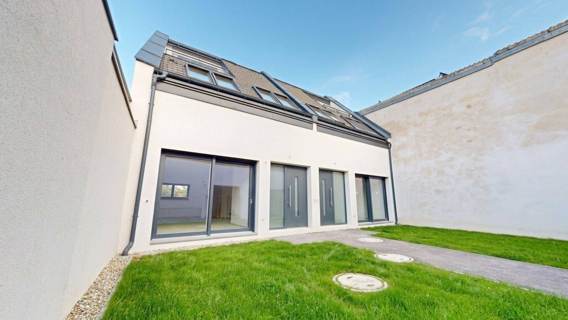 Seitenansicht einer modernen Neubau-Doppelhaushälfte mit großen Fenstern und Dachschrägen.