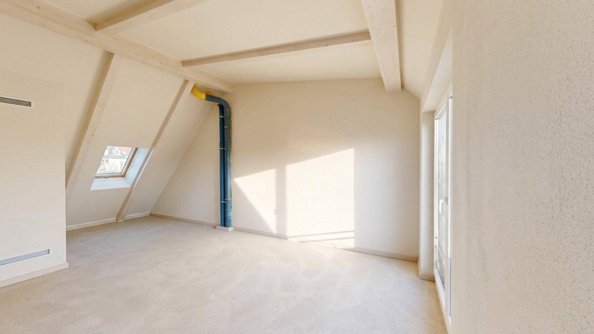 Unfertiger Dachgeschossraum mit sichtbaren Holzbalken, Dachfenster und viel Sonneneinstrahlung.