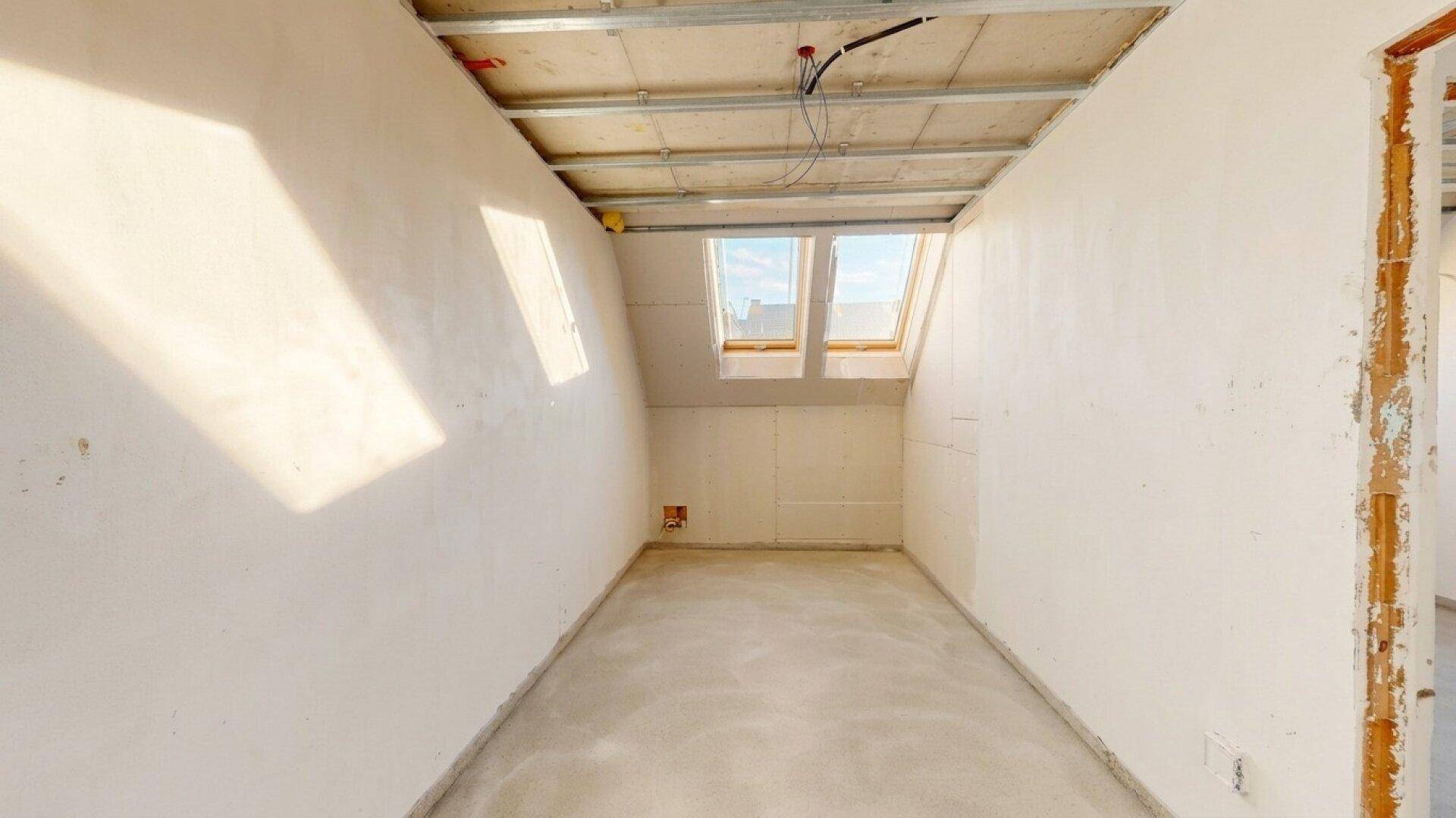Unfertiger Raum im Dachgeschoss mit zwei Dachfenstern und sichtbarer Deckenkonstruktion.