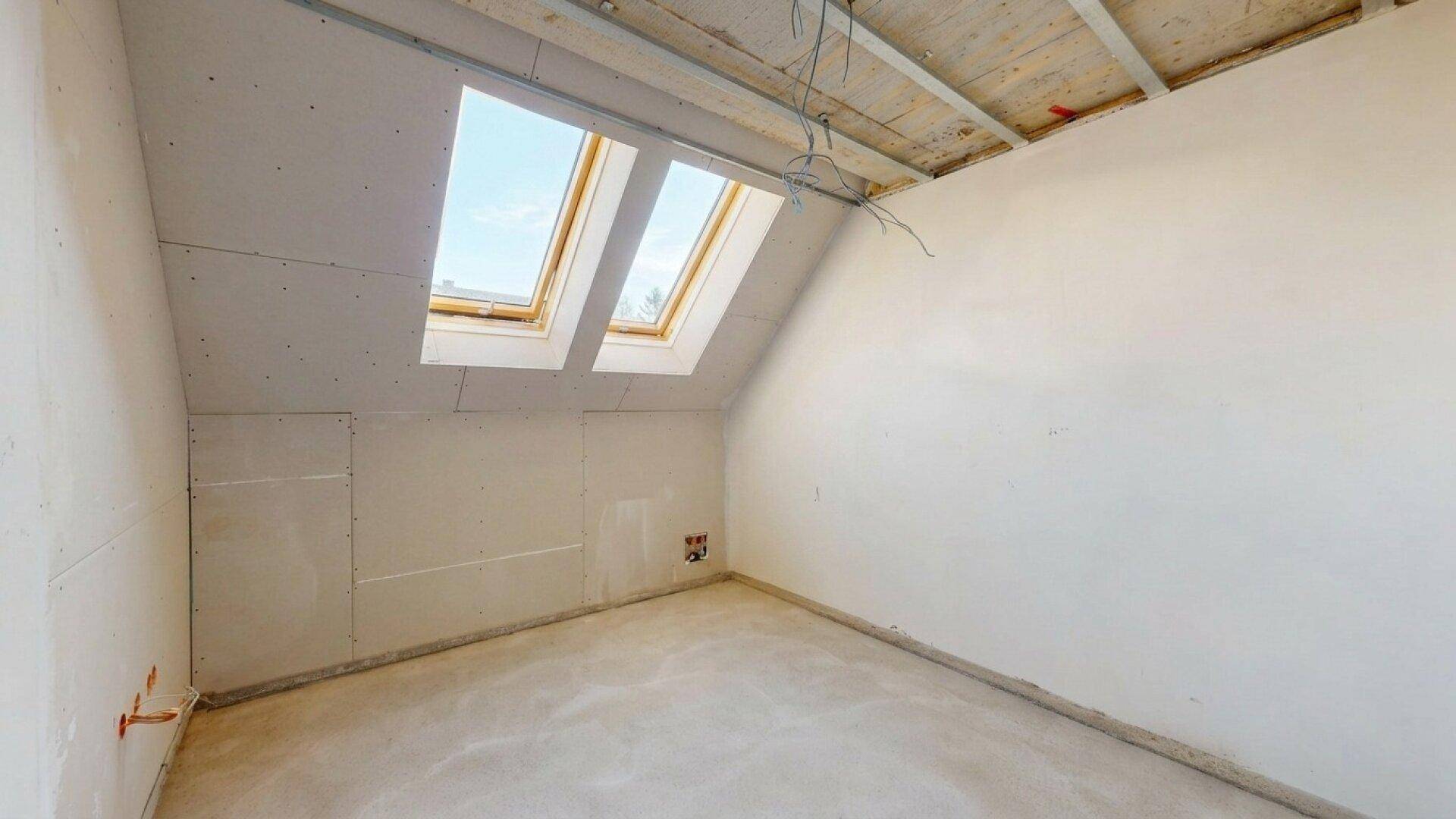Heller Dachgeschossraum im Rohbau mit zwei großen Dachfenstern für optimale Belichtung.
