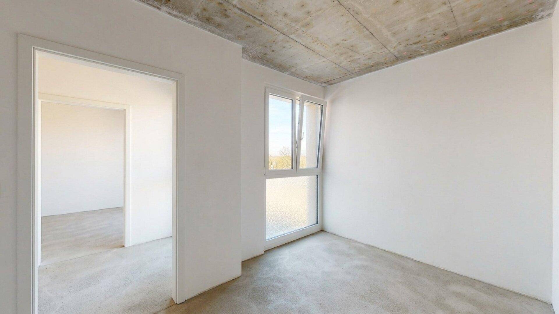 Unfertiger Raum mit sichtbarer Beton-Decke und großem Fenster für natürliches Licht.