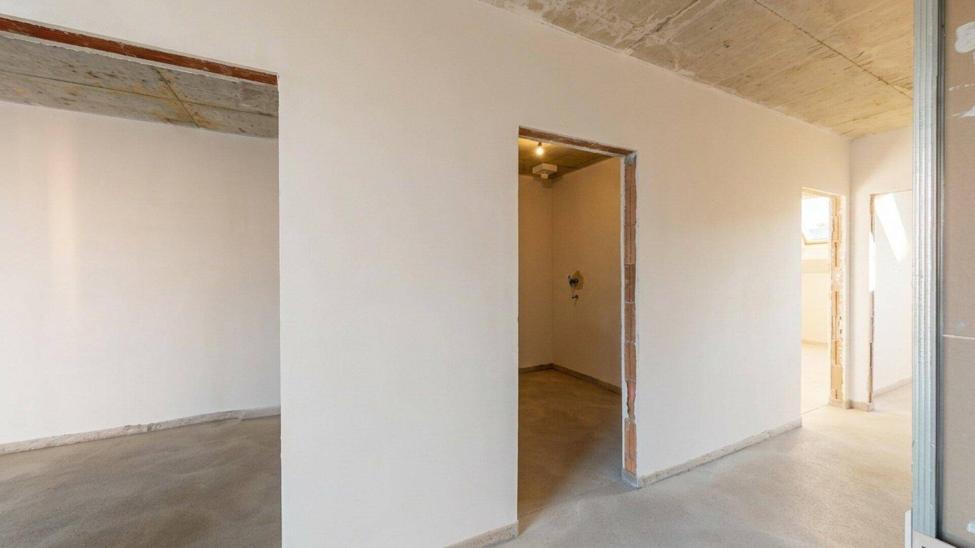 Unfertiger Flurbereich mit sichtbarer Beton-Decke und Durchgängen zu weiteren Räumen.