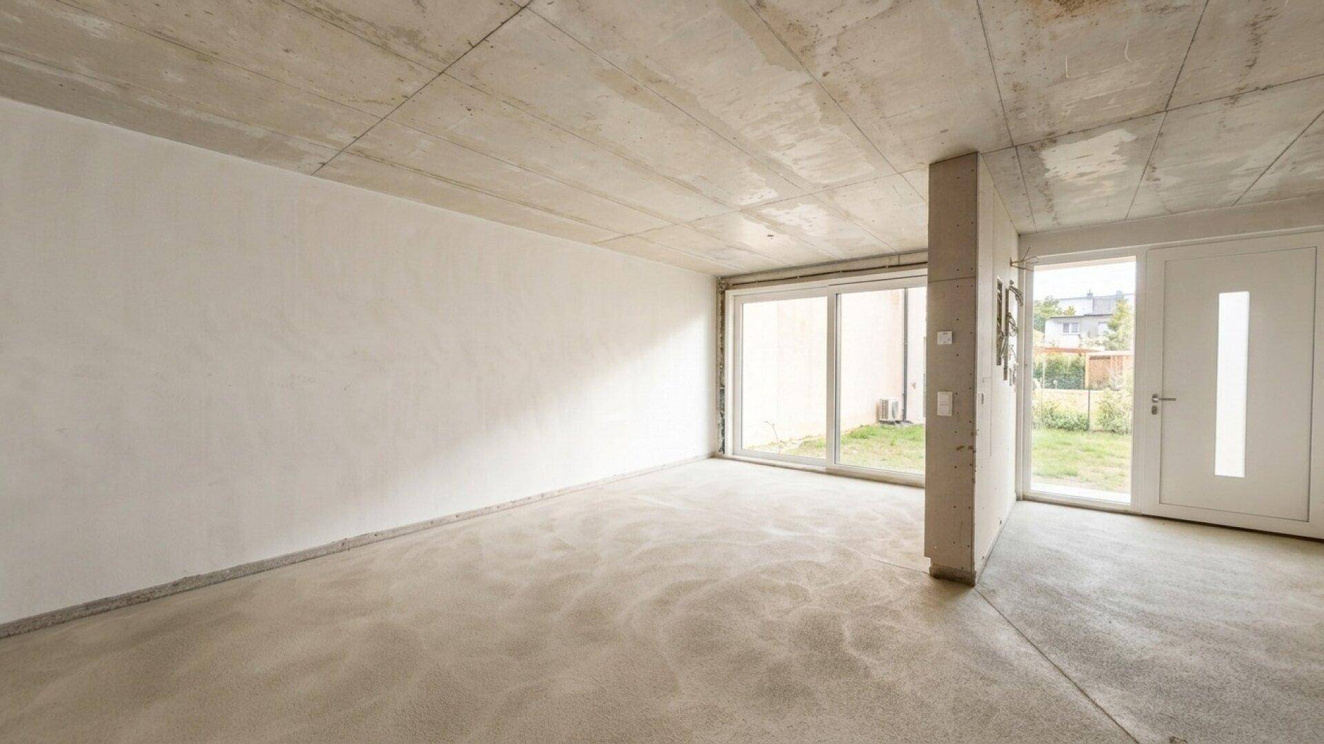Heller Erdgeschossraum im Rohbau mit Eingangstür und direktem Gartenzugang.