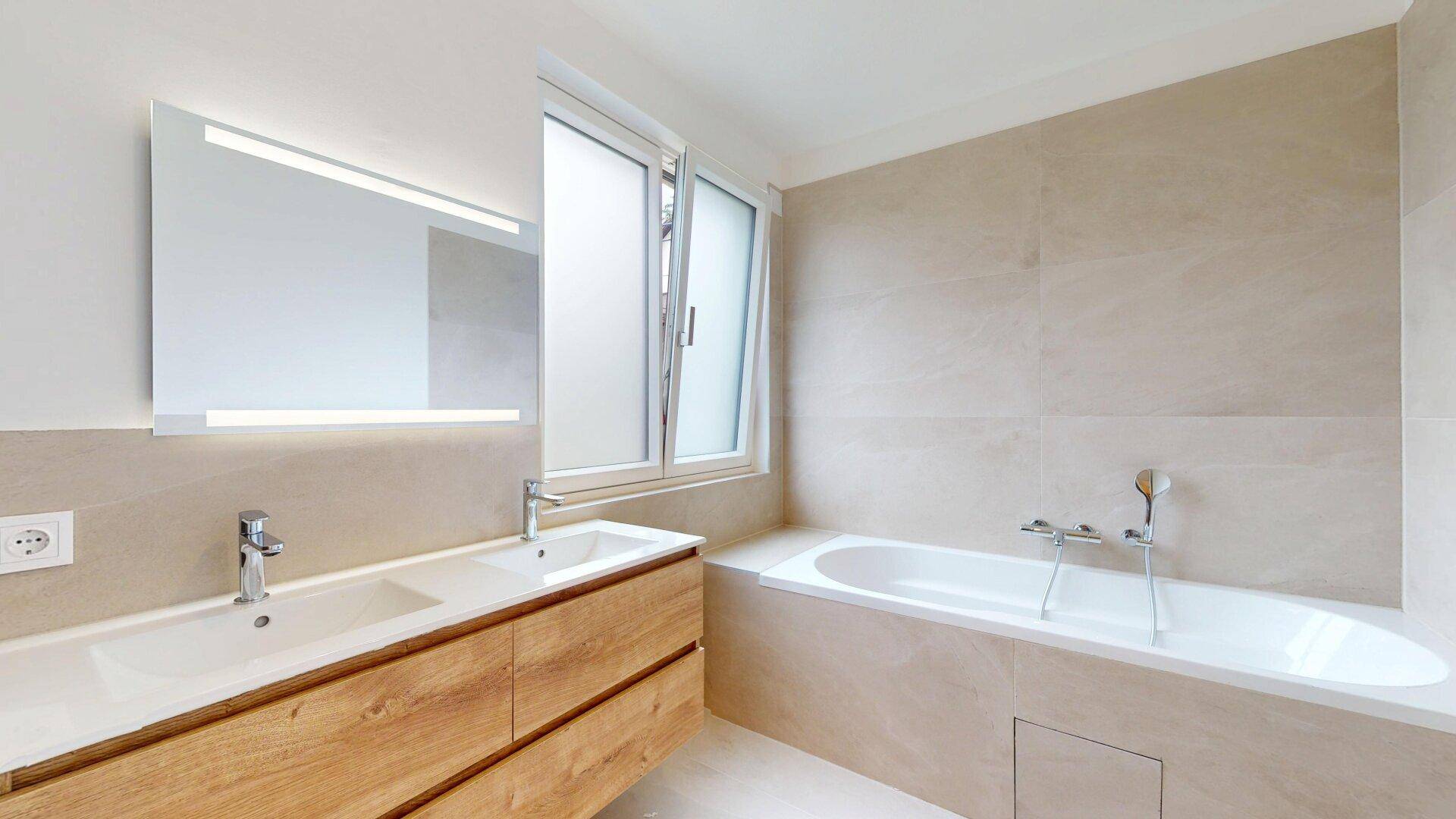 Modernes Badezimmer mit Doppelwaschbecken, Badewanne und großformatigen Fliesen.