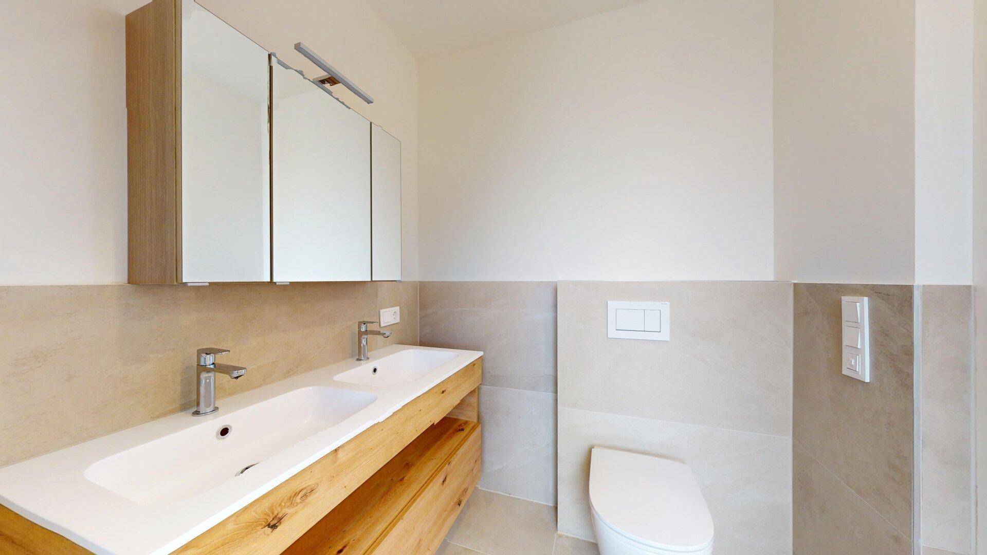 Modernes Badezimmer mit Doppelwaschbecken, Wand-WC und großformatigen Fliesen.