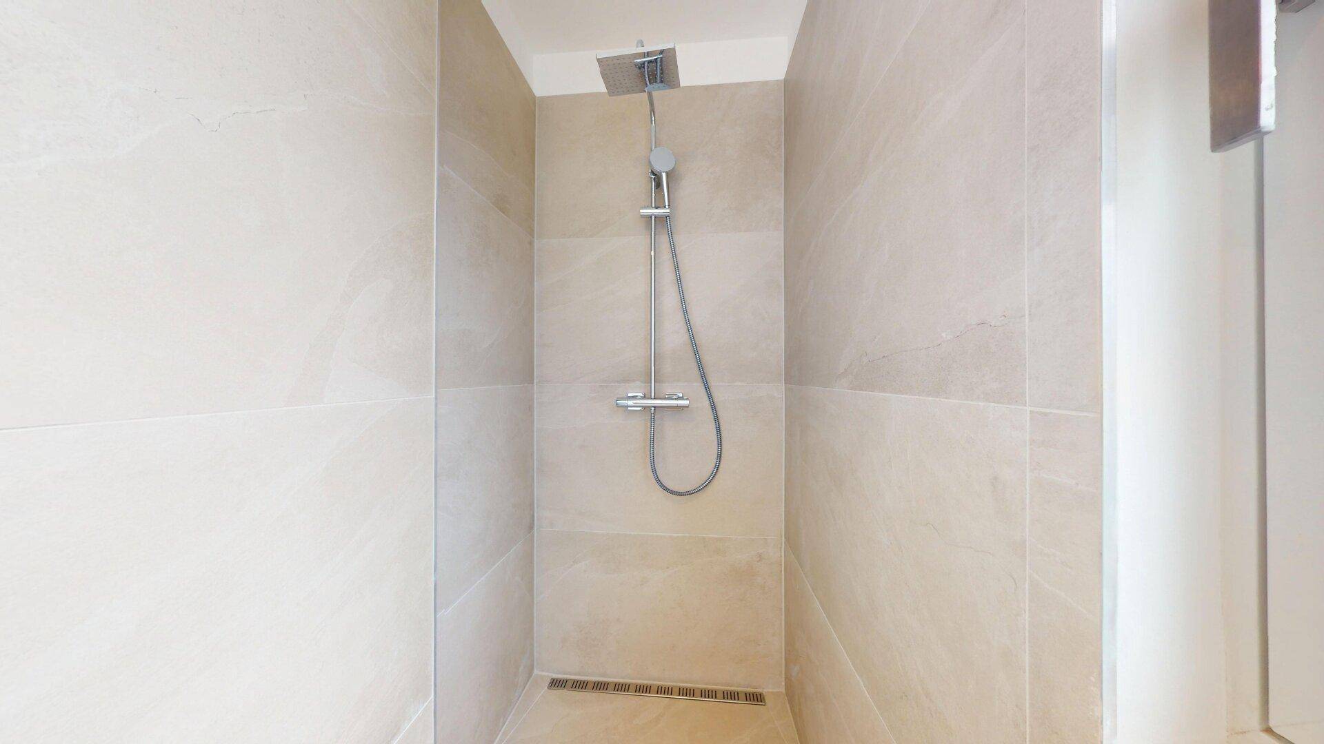 Ebenerdige Dusche mit Regenduschkopf und modernen, hellen Fliesen an den Wänden.