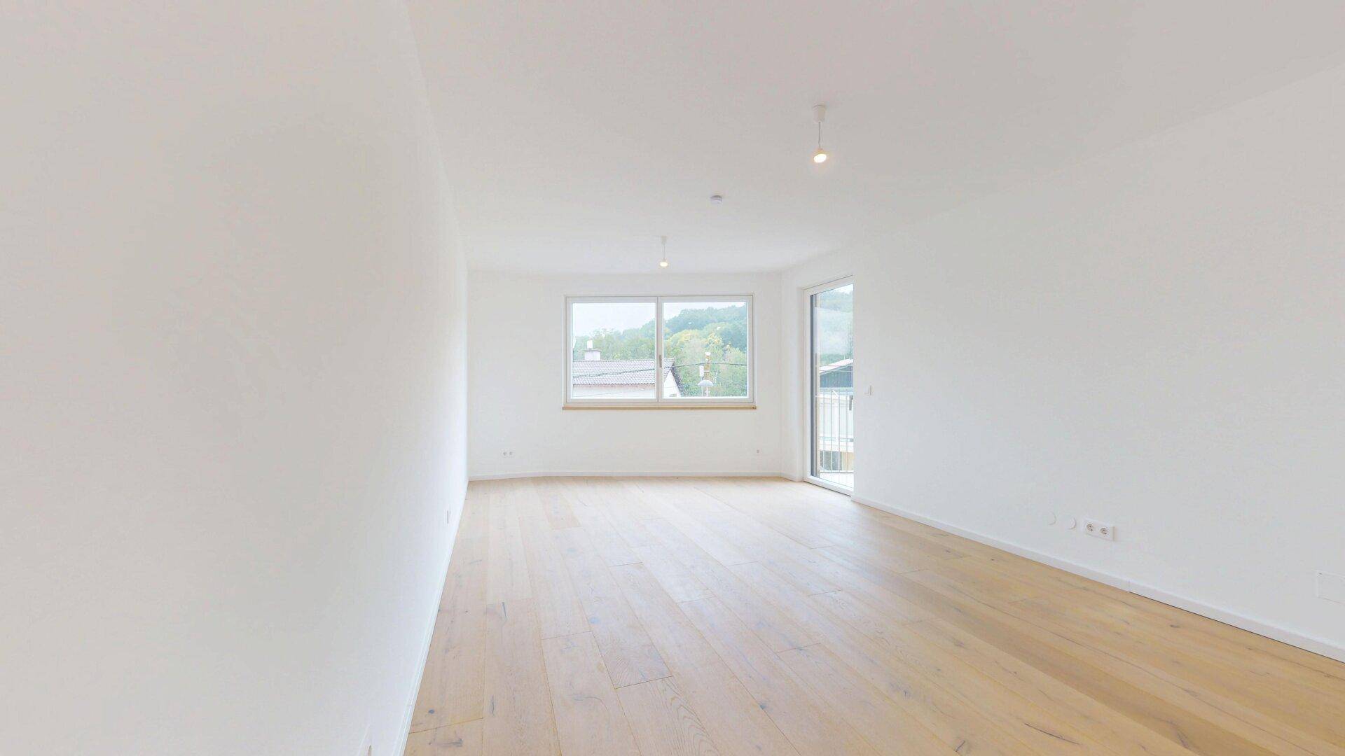 Helles Zimmer mit Holzboden und Zugang zu einem Balkon oder einer kleinen Terrasse.