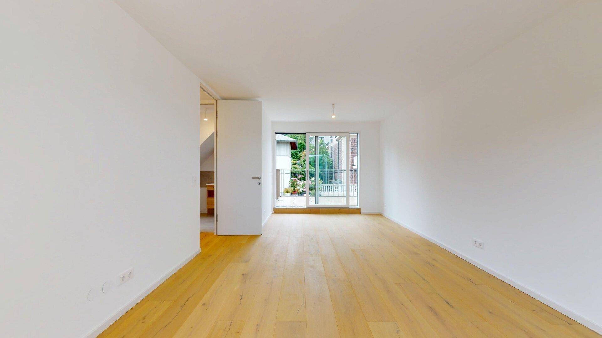 Geräumiges Zimmer mit Holzboden und Schiebetür, die zu einem Außenbereich führt.