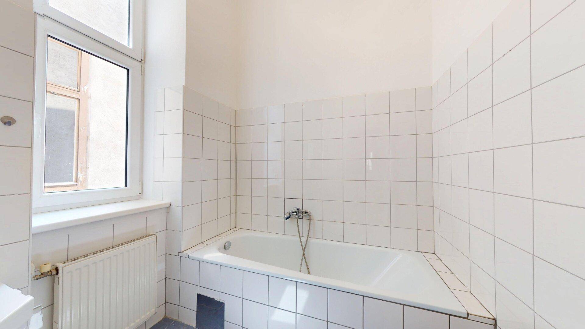 Badezimmer mit weißen Fliesen, Badewanne, Fenster und Heizkörper.