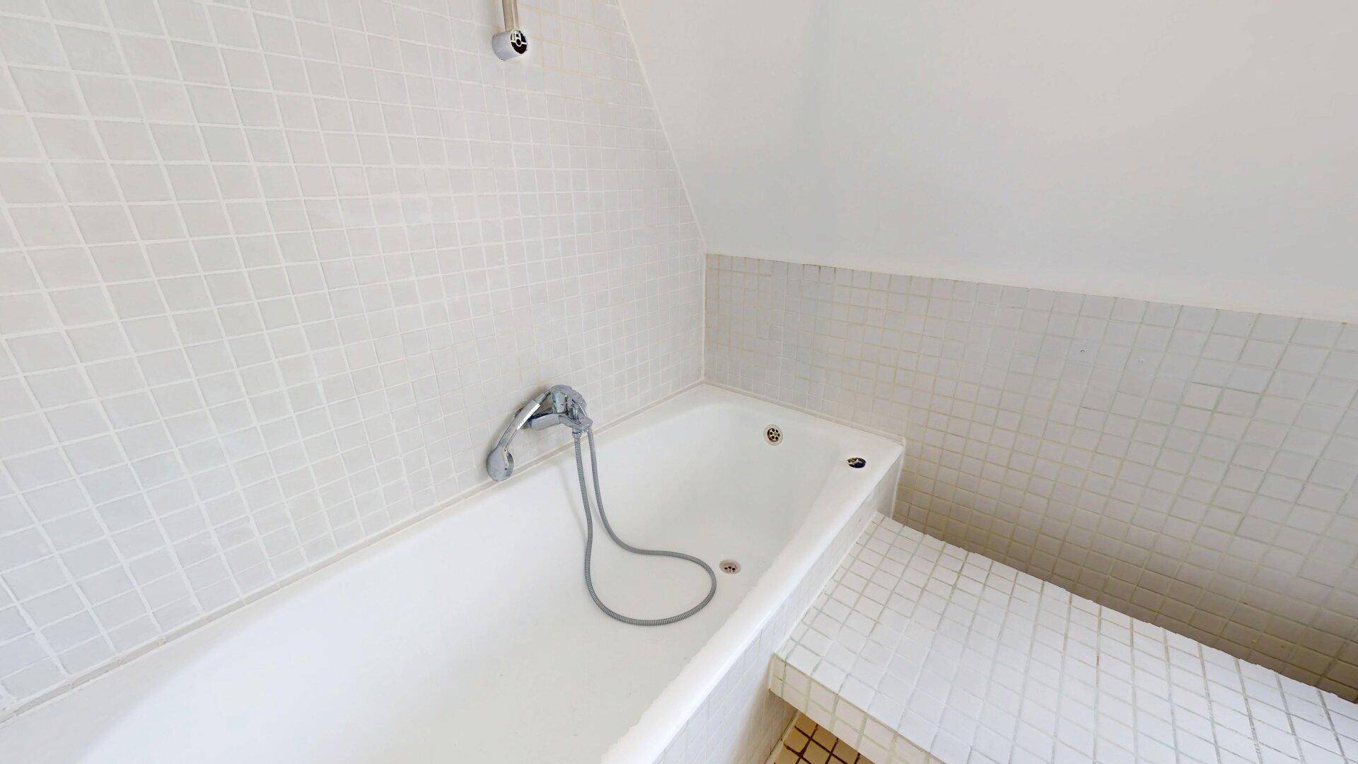 Helles Badezimmer mit Badewanne, weißen Fliesen und Dachschräge, das eine gemütliche Atmosphäre schafft.