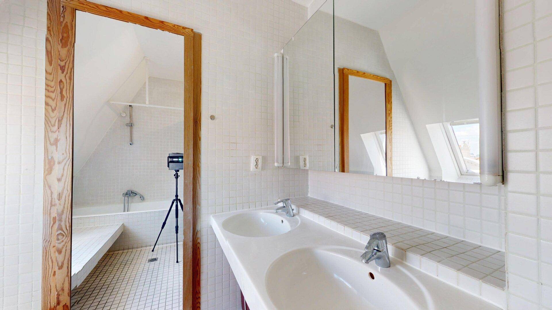 Badezimmer mit Doppelwaschbecken, Spiegelschrank und Blick auf die Badewanne unter der Dachschräge.