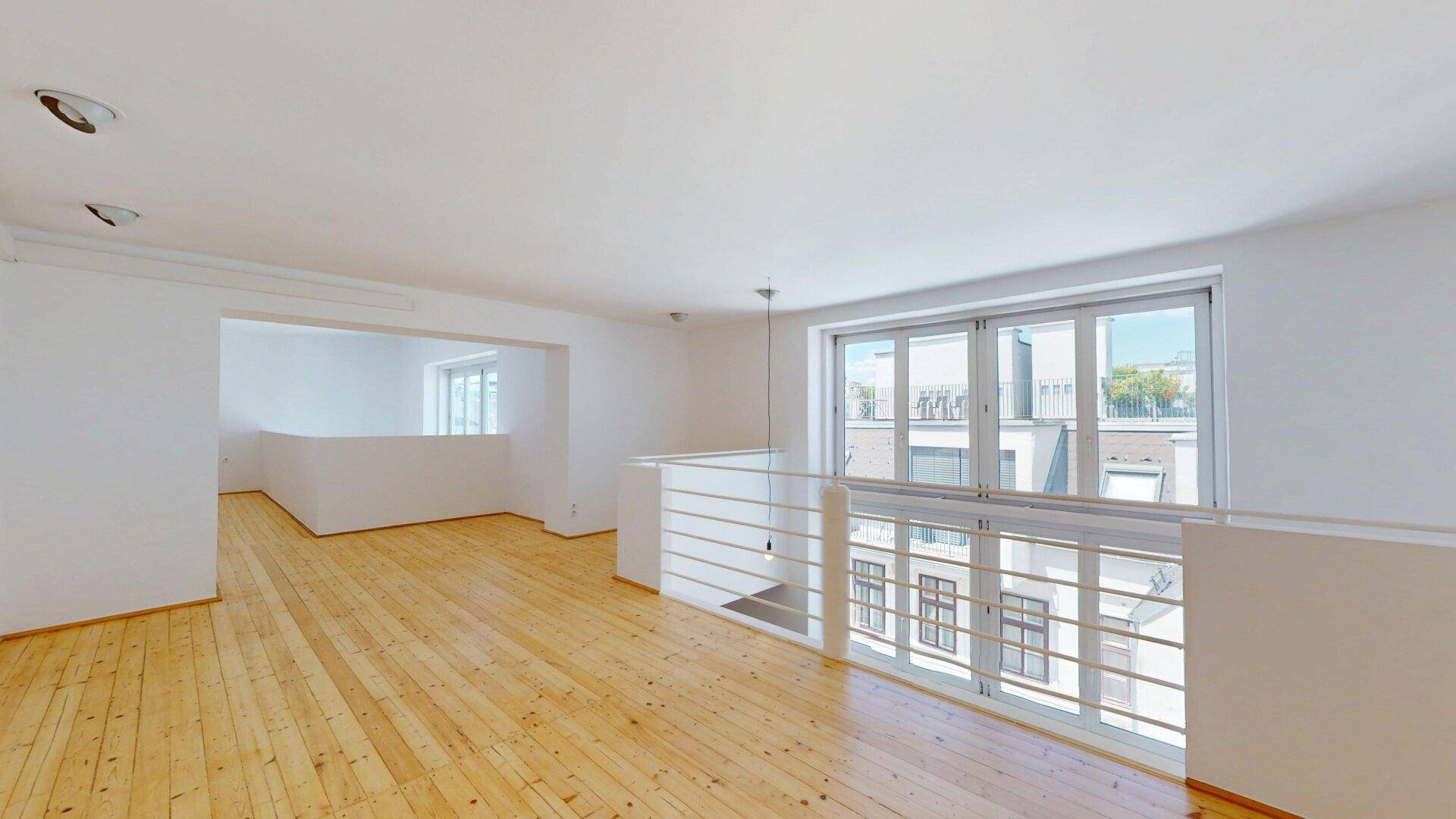 Offener Galeriebereich mit Holzplankenboden, großen Fenstern und Blick auf den unteren Wohnbereich.