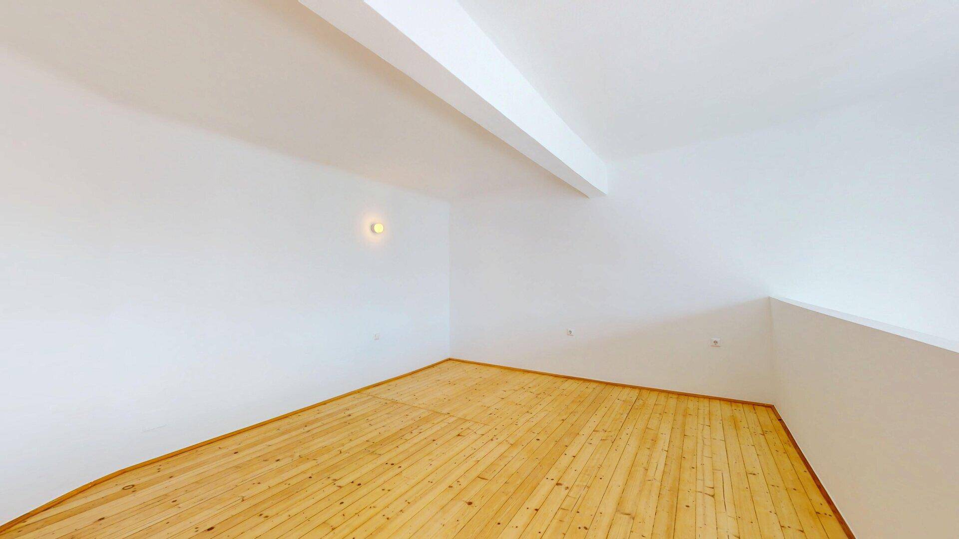 Gemütlicher Raum im Dachgeschoss mit Holzplankenboden, weiß gestrichenen Wänden und Dachschräge.