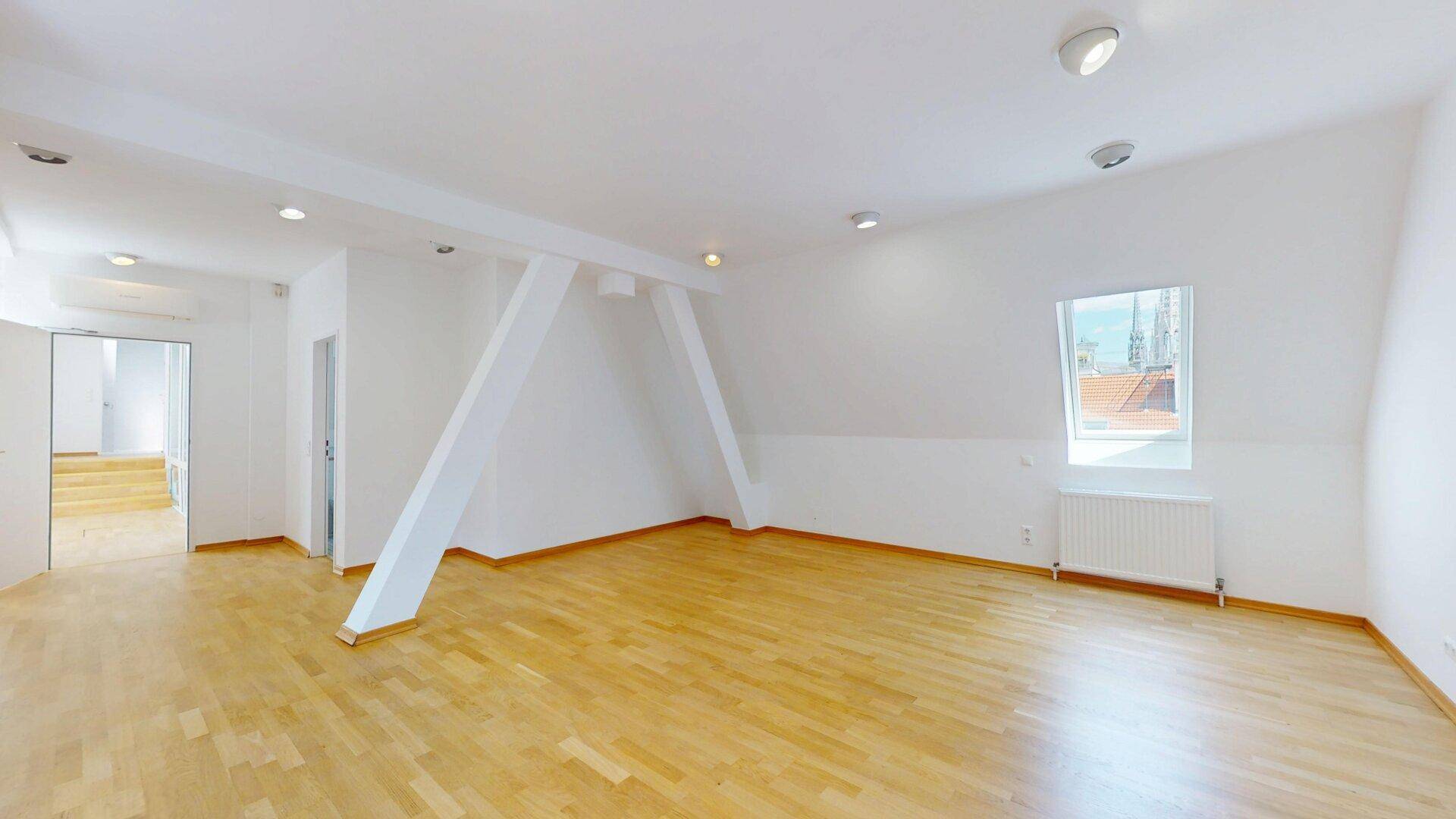 Geräumiger Wohnraum mit Holzfußboden, Dachschräge, sichtbaren Balken und Einbaustrahlern.