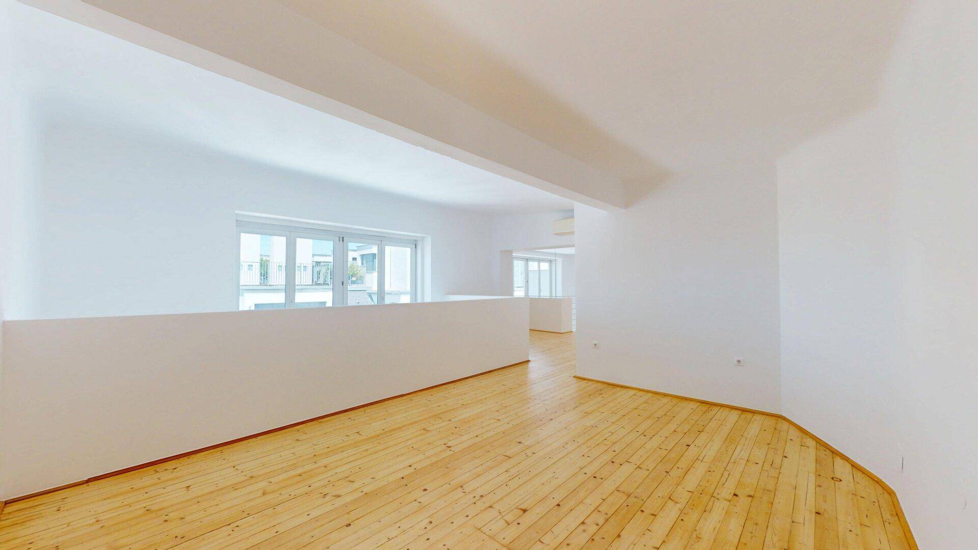 Offener Bereich im Obergeschoss mit Holzplankenboden, weißem Geländer und großen Fenstern.