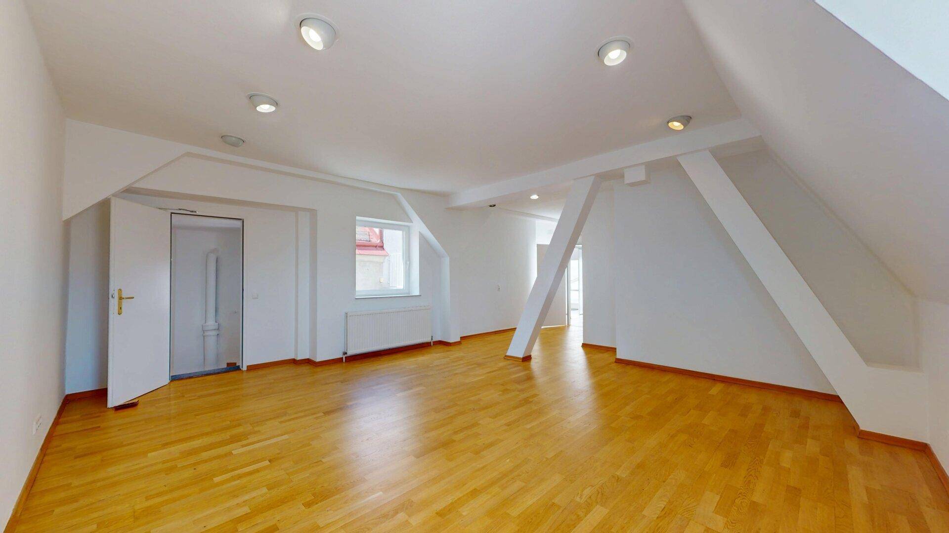 Heller Wohnraum mit Holzfußboden, Dachschräge, sichtbaren Balken und Einbaustrahlern.
