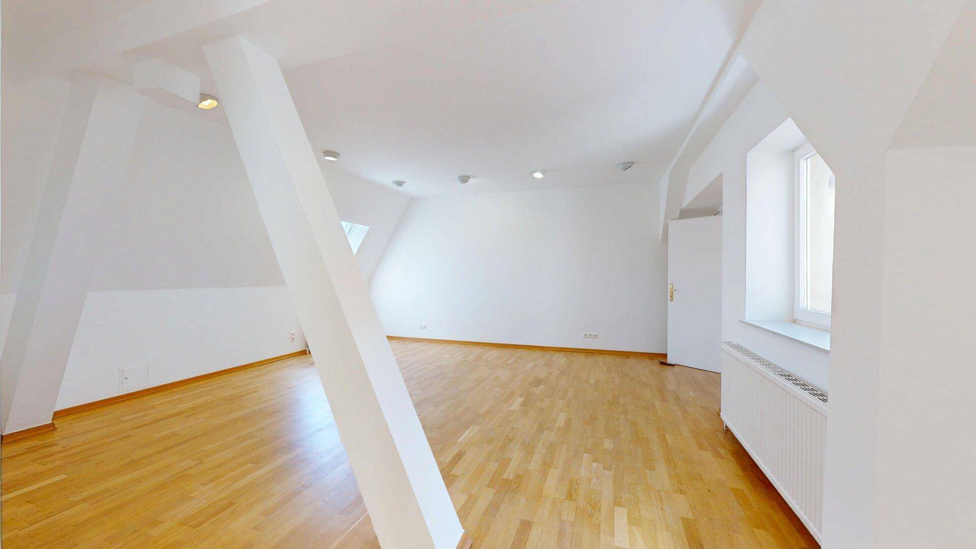 Geräumiger Wohnraum mit Holzfußboden, Dachschräge, sichtbarem Balken und Einbaustrahlern.