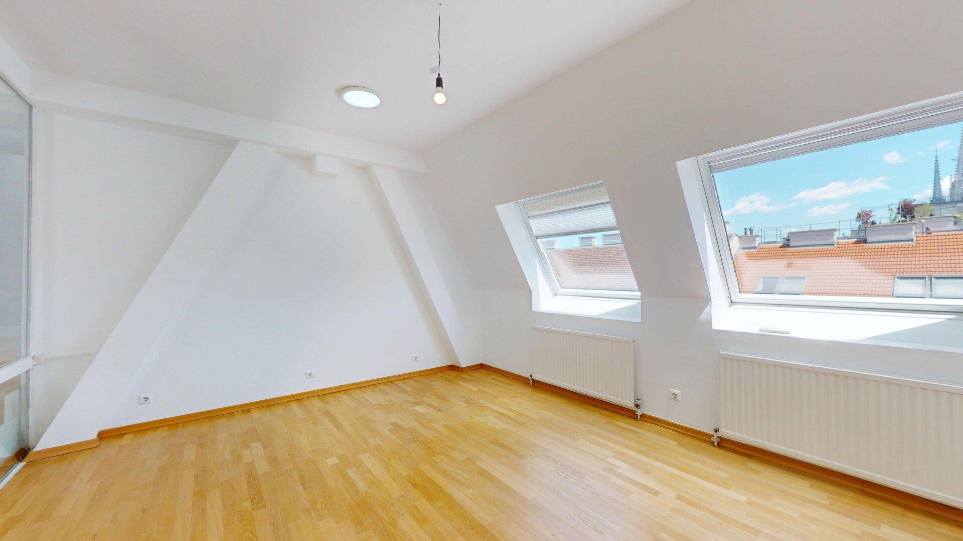 Helles Schlafzimmer mit Holzfußboden, Dachschräge, Dachfenstern und Blick über die Stadt.