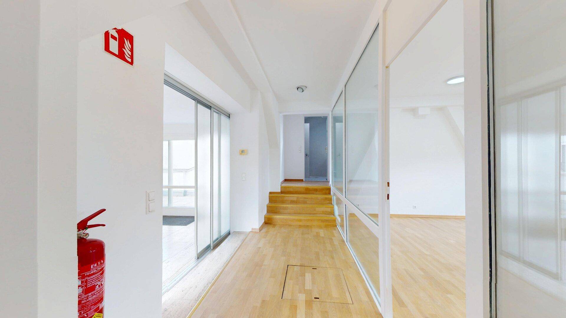 Heller Flur mit Holzfußboden, Glasabtrennung, Schiebetür und Treppe zum oberen Bereich.