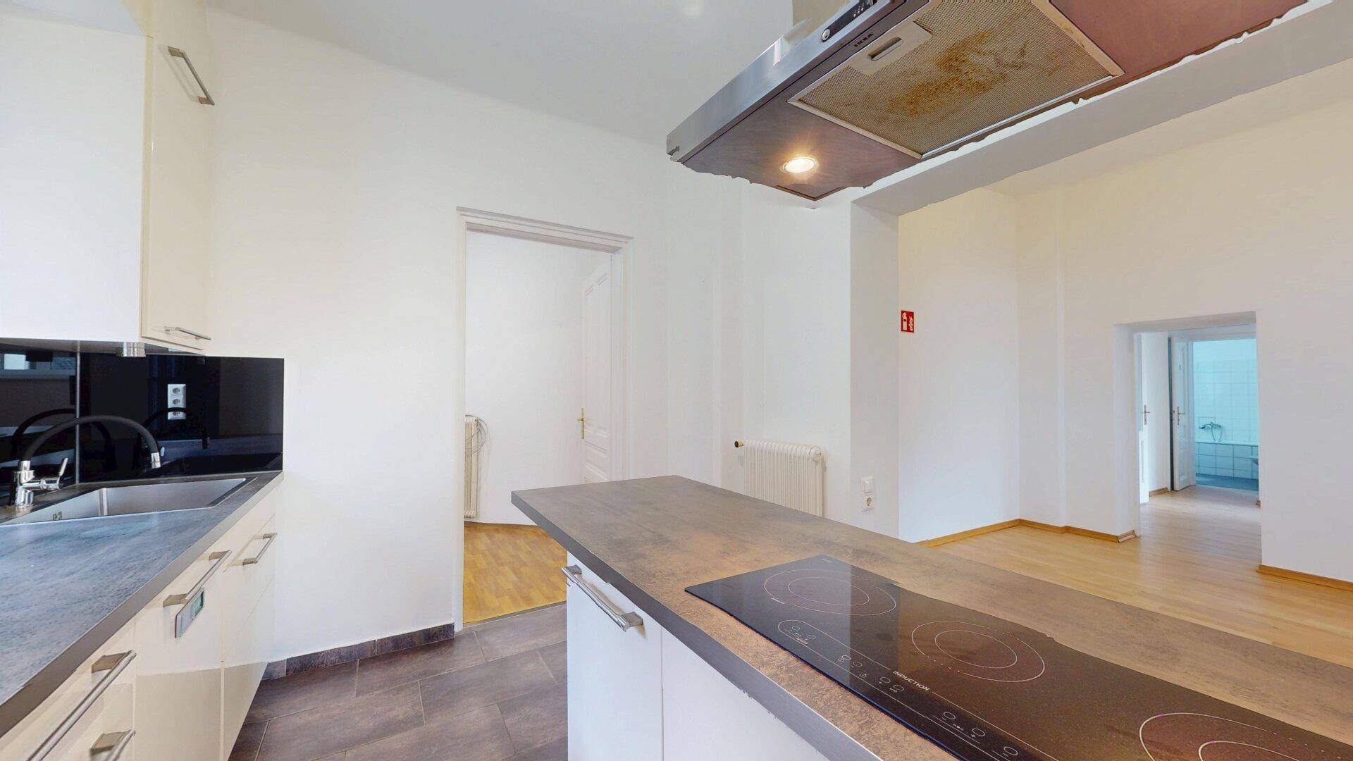 Moderne Küche mit weißen Schränken, dunkler Arbeitsplatte, Induktionskochfeld und Dunstabzugshaube.