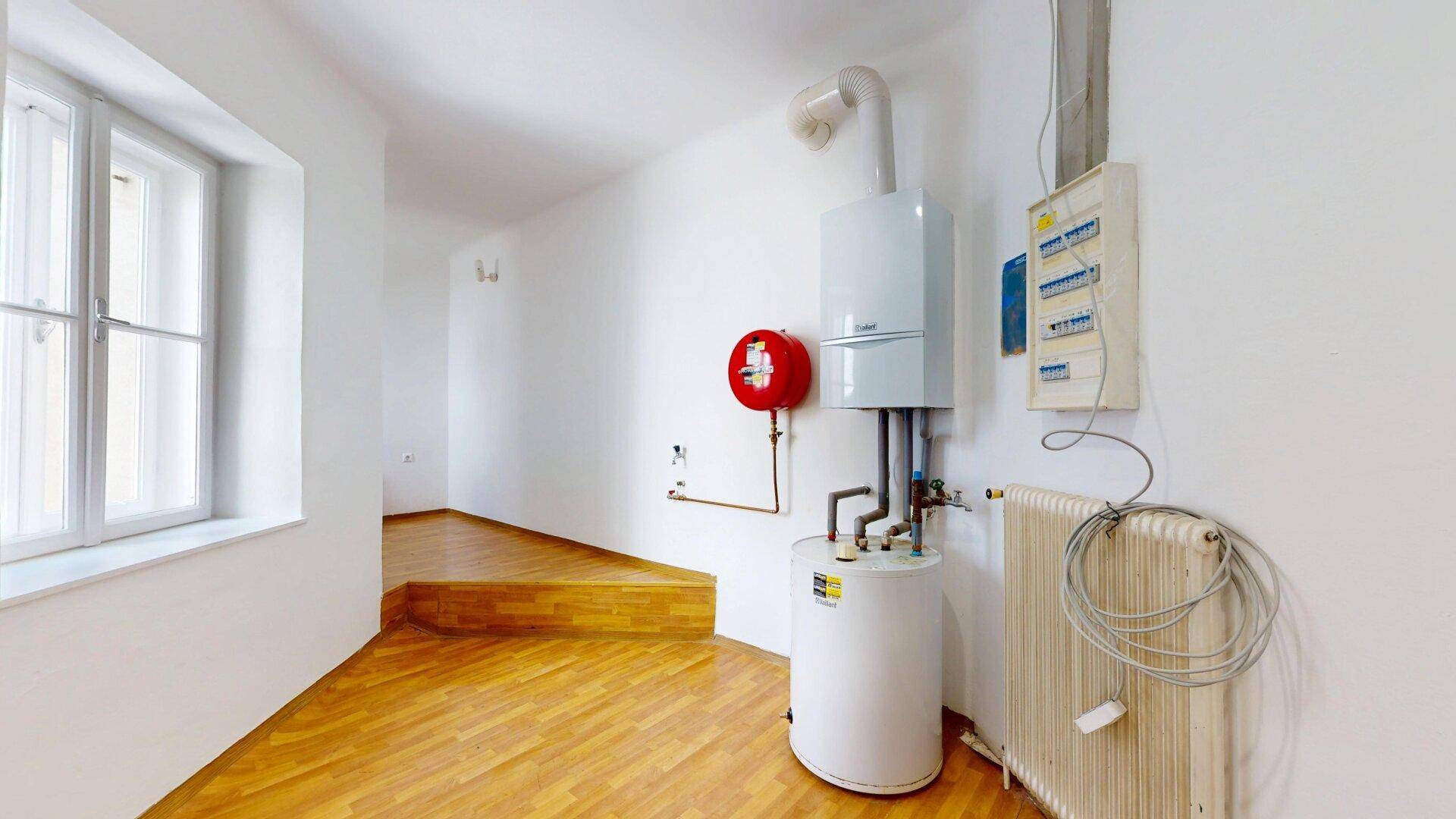 Hauswirtschaftsraum mit Warmwasserbereiter, Heizkessel, Heizkörper und einem Fenster, ausgestattet mit Holzfußboden.