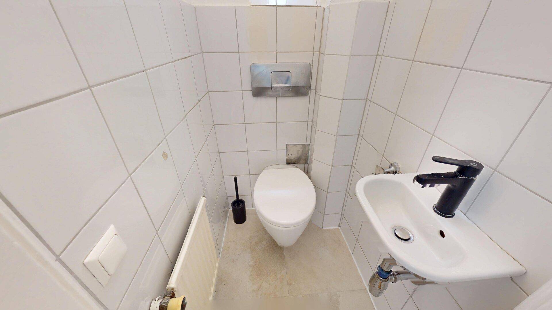 Kleines Gäste-WC mit Toilette, Handwaschbecken und Heizkörper, komplett gefliest in Weiß.