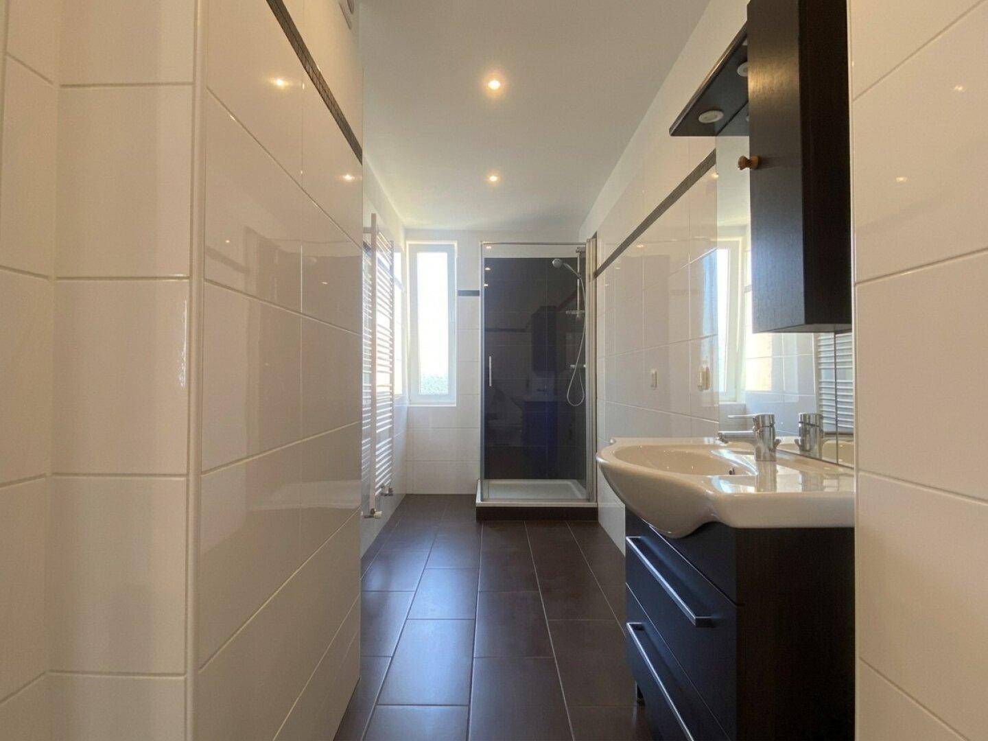 Langes Badezimmer mit begehbarer Dusche, Waschtisch und beheiztem Handtuchhalter.