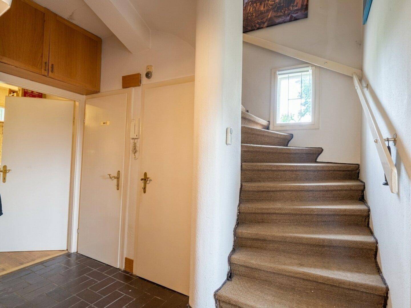 Flur mit dunklem Fliesenboden und einer Teppich-Wendeltreppe, die in die oberen Stockwerke führt.