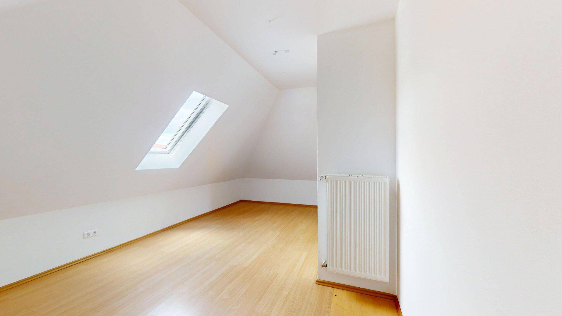 Helles Dachzimmer mit Laminatboden, Heizkörper und einem schrägen Dachfenster.