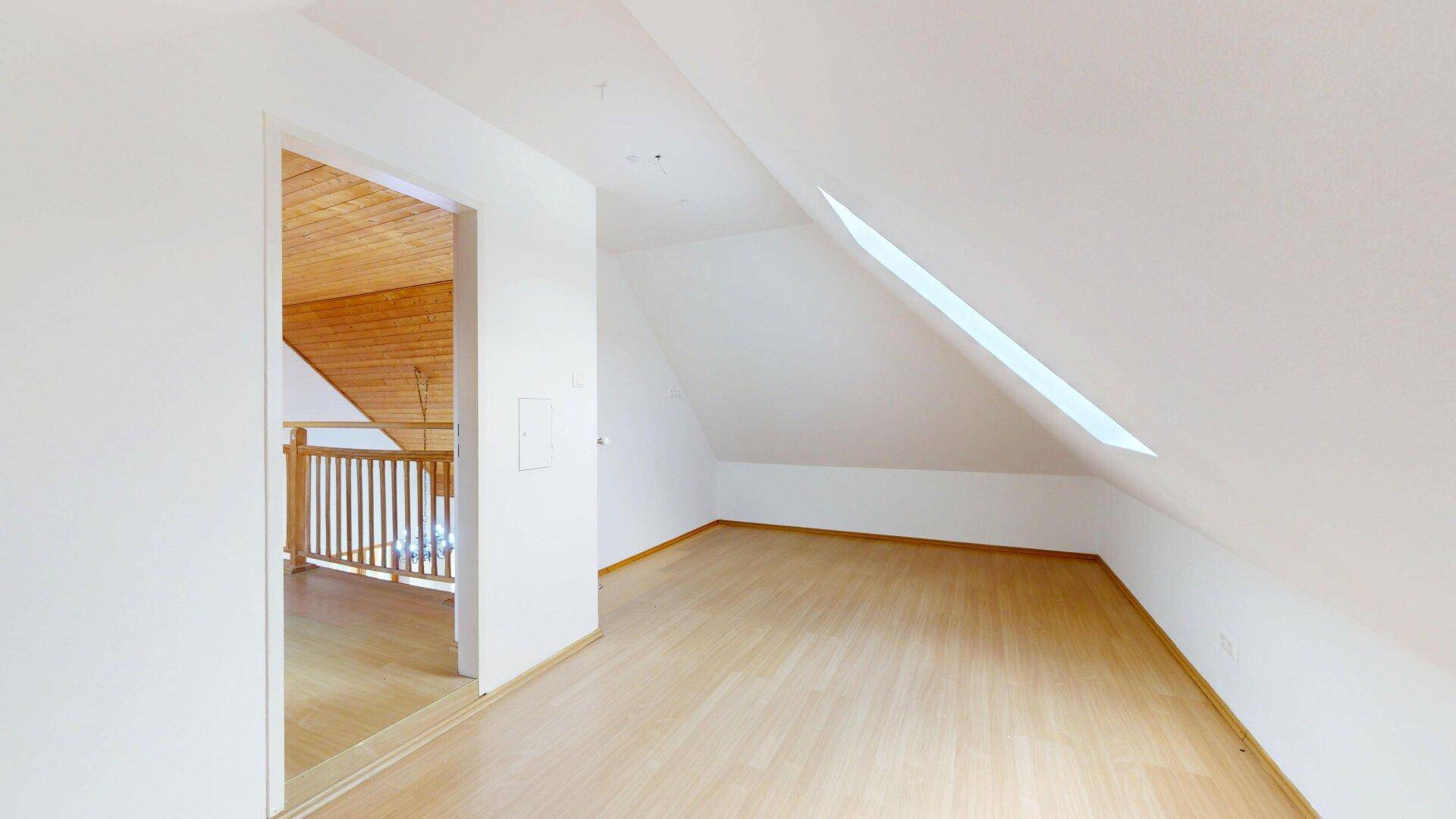 Dachzimmer mit Laminatboden, weißen Wänden und einem Dachfenster für natürliches Licht.